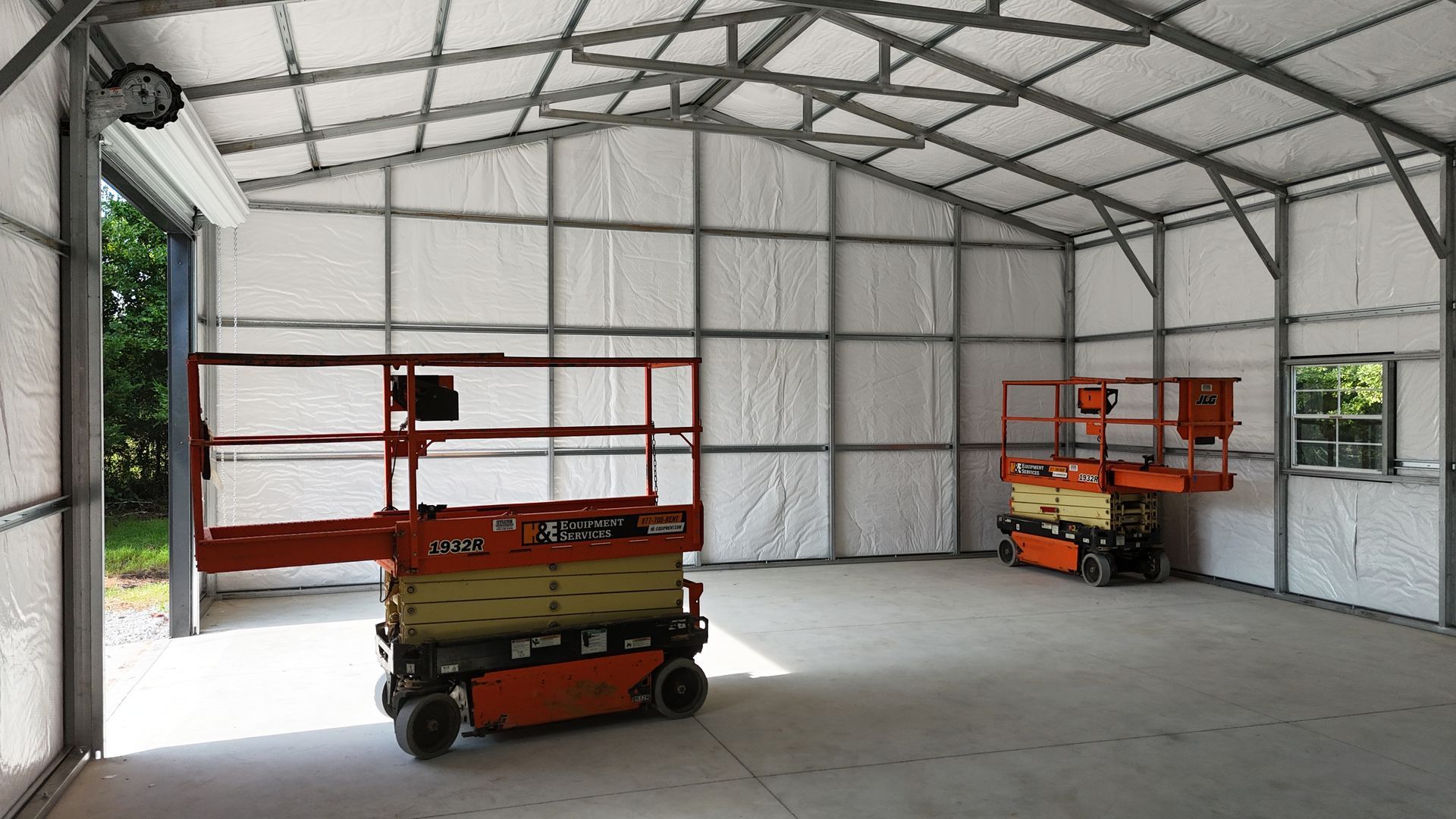 Empty warehouse with two orange scissor lifts inside a metal-framed building