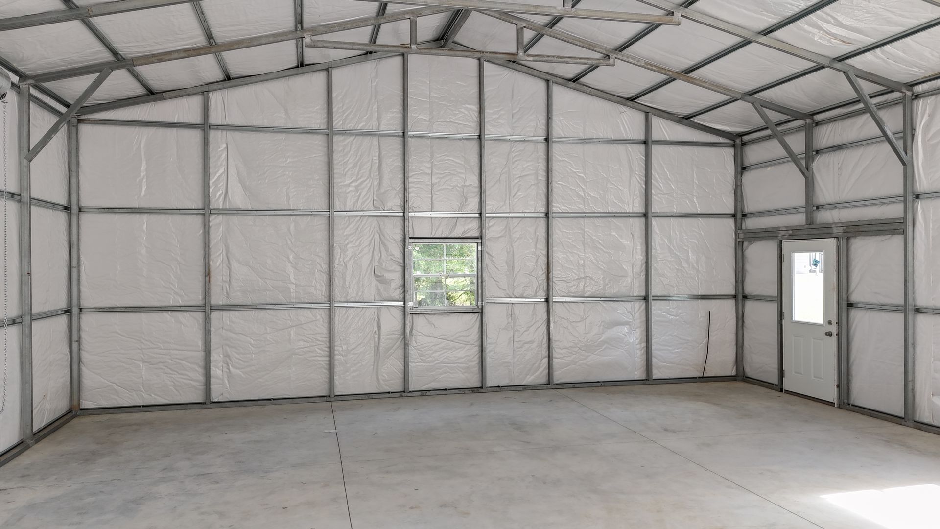 Empty metal-framed warehouse interior with white insulated walls and concrete floor, lit by a small central window.
