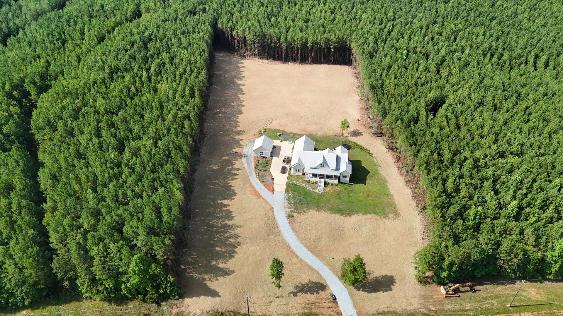 Aerial view of a white house with a winding driveway, surrounded by dense green forest and open yard.