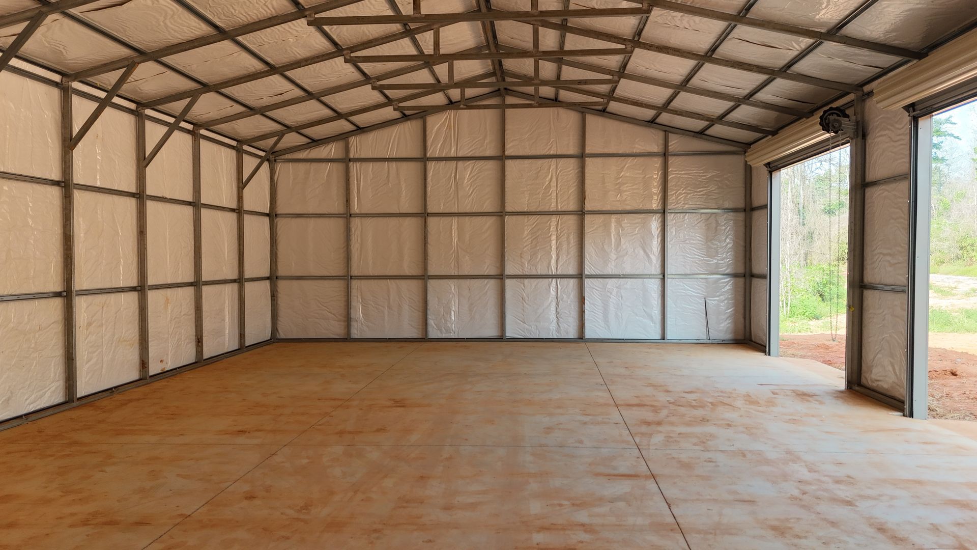 Empty metal warehouse with plywood walls, a concrete floor, and an open doorway to the outside