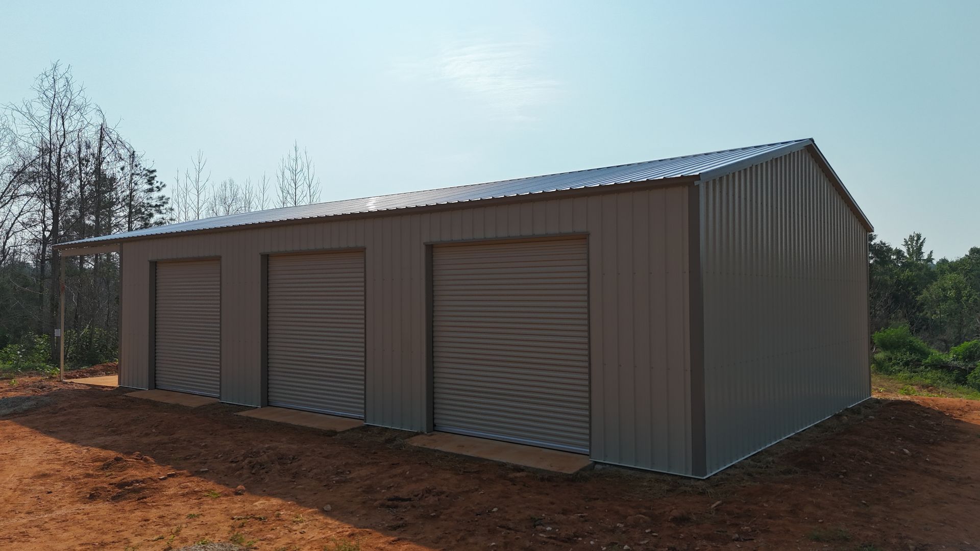 Gray metal storage building with roll-up doors on a dirt lot under a clear sky