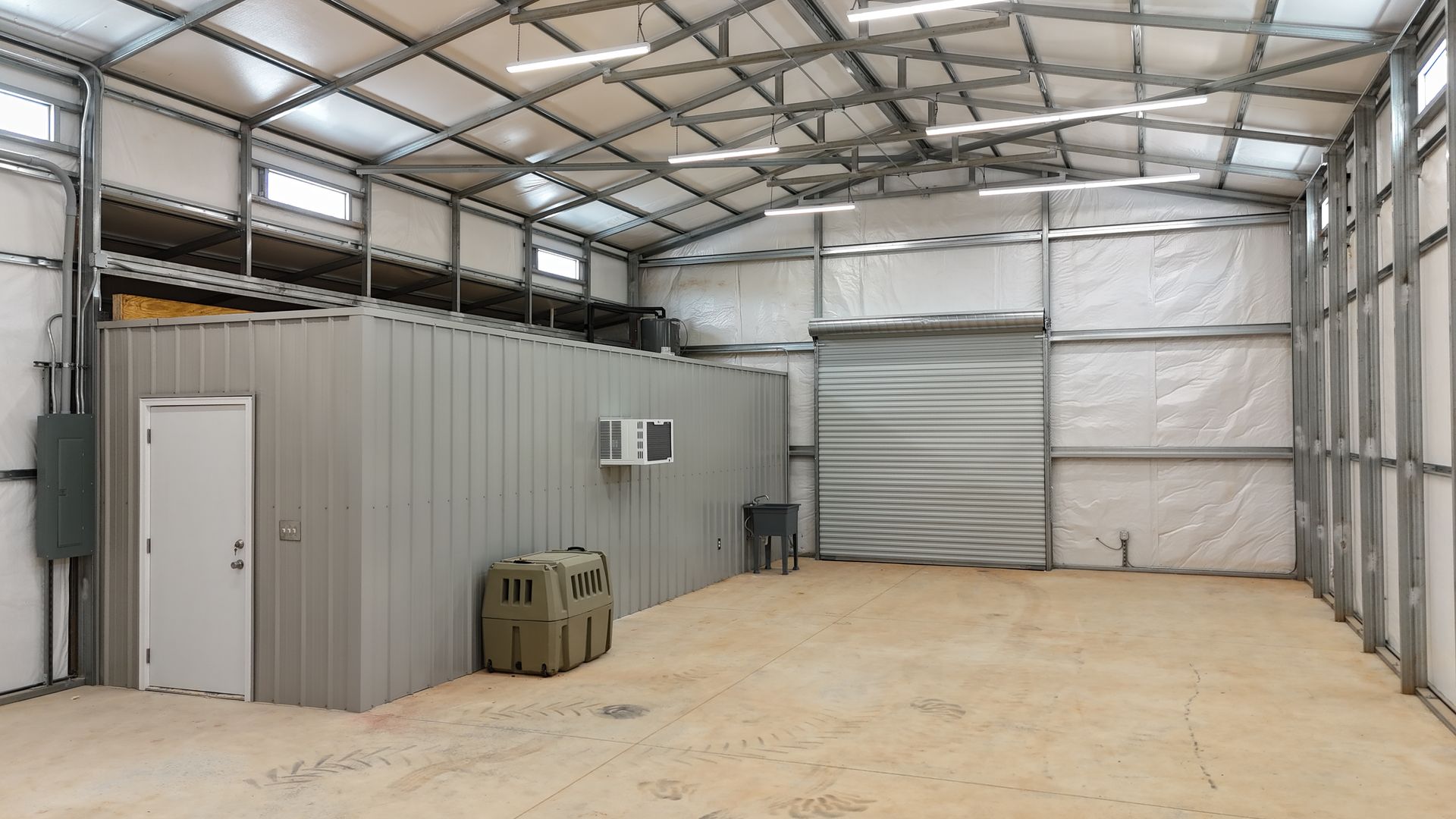 Empty industrial warehouse with metal walls, roll-up door, and concrete floor under a high steel roof