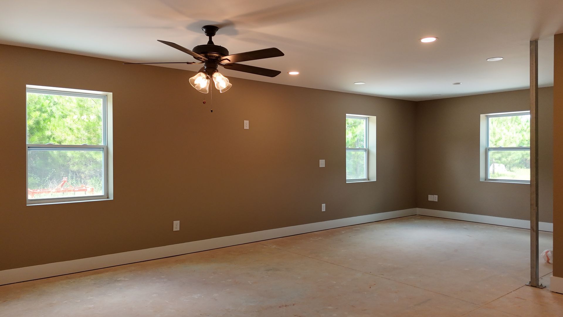 Empty beige living room with carpet, ceiling fan, recessed lights, and three windows