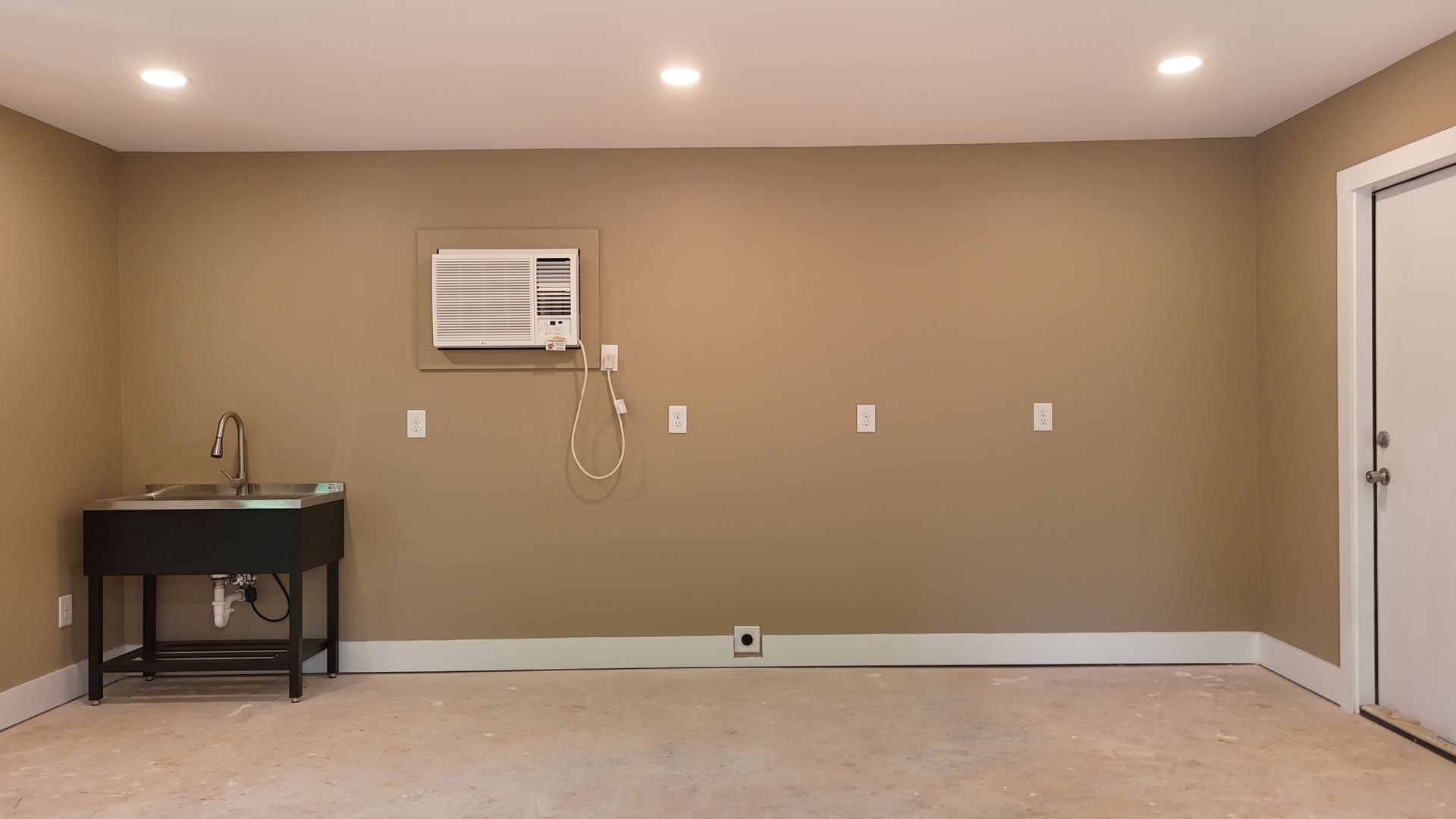 Empty beige room with carpet, wall-mounted air conditioner, black sink cabinet, and white door
