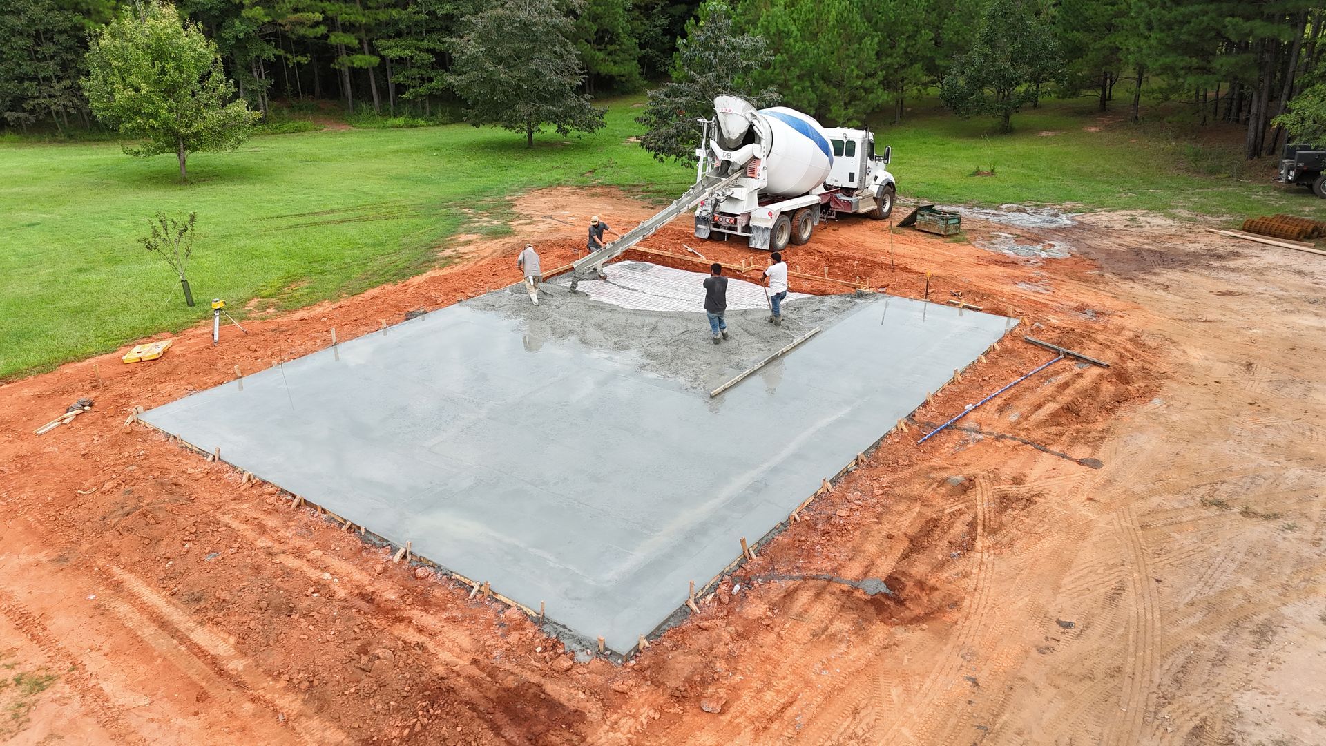 Concrete being poured on a rectangular slab by a construction machine at a building site.