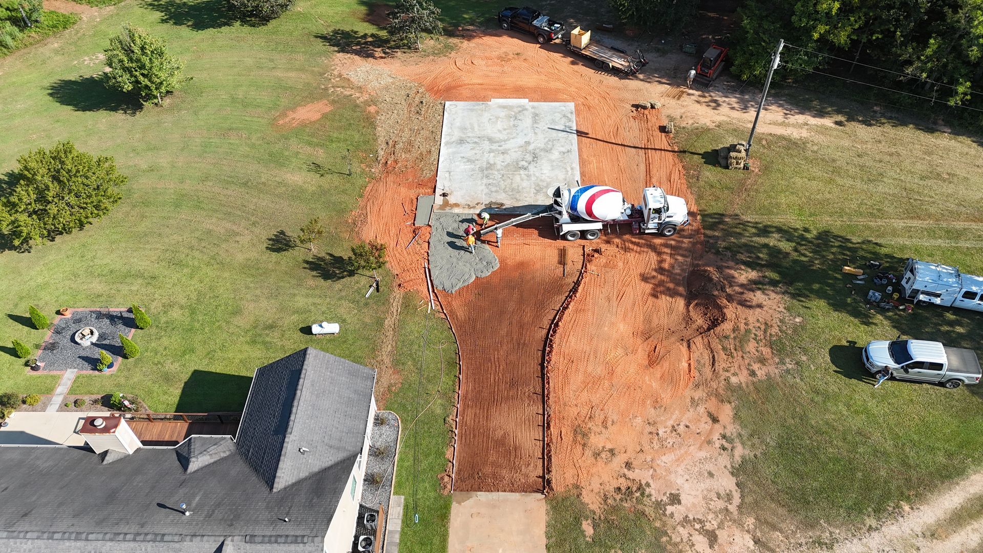Aerial view of a house foundation excavation with orange dirt, concrete slab, and a truck parked nearby.