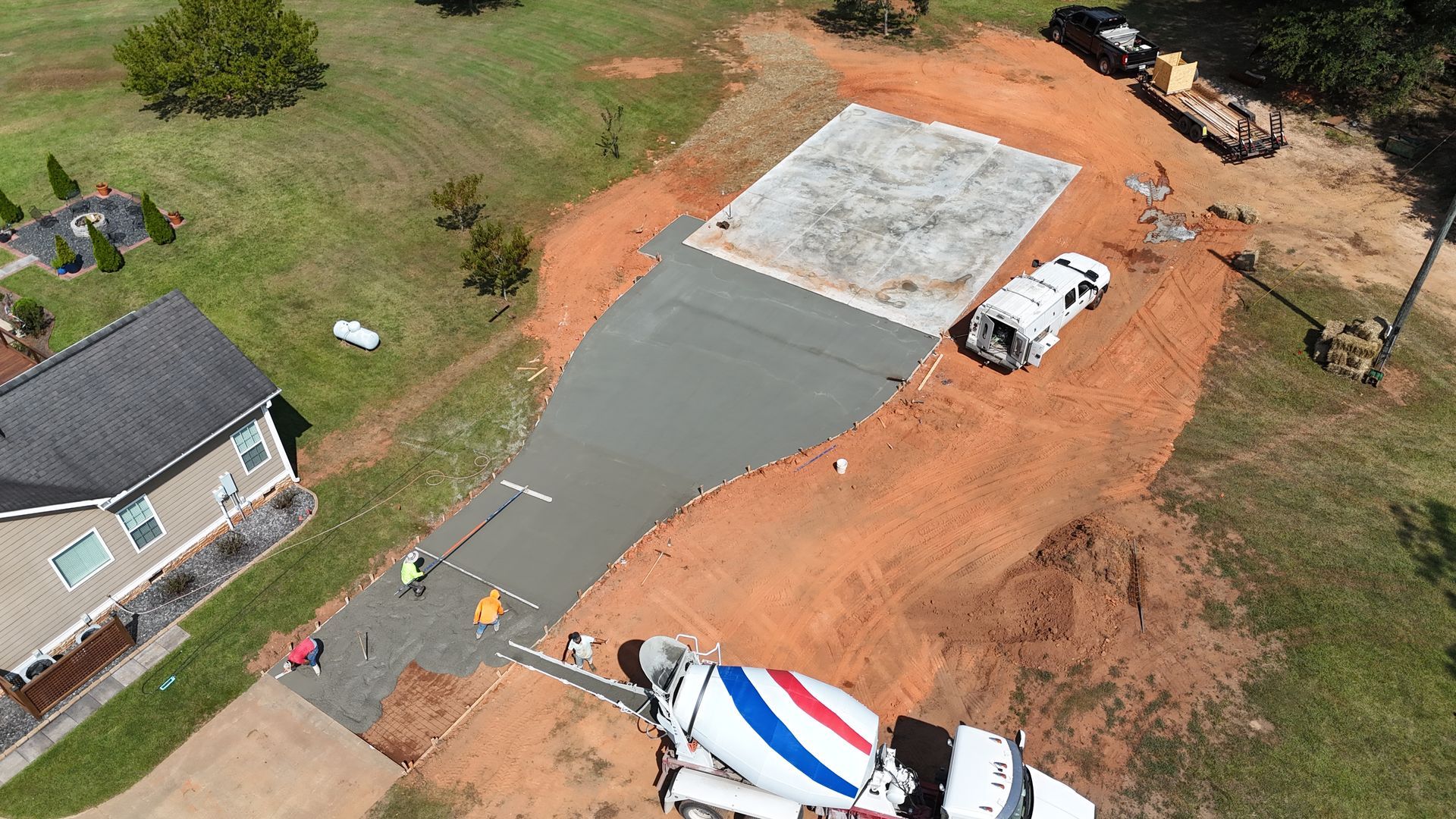 Aerial view of a house driveway under construction with concrete, dirt, and work trucks.