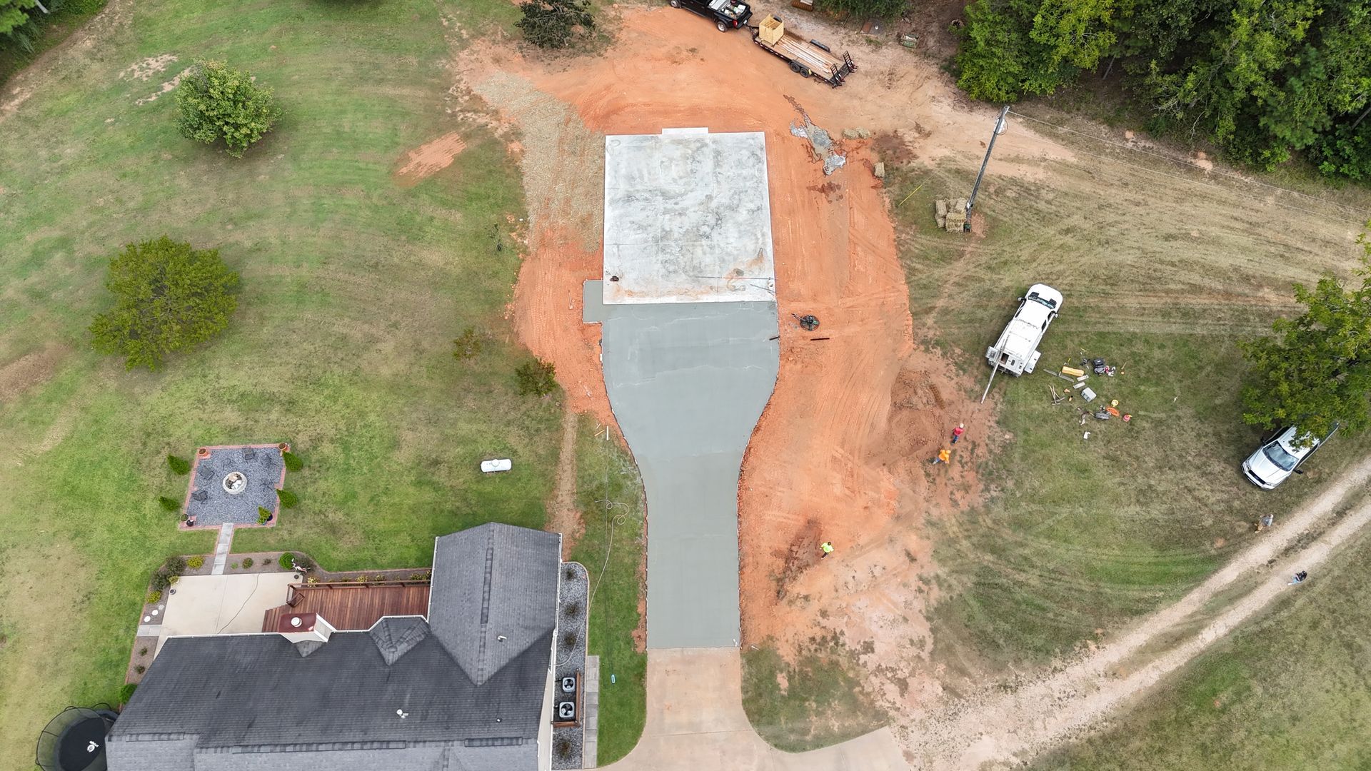 Aerial view of a house with a new gray driveway and concrete slab beside orange dirt and grassy yard.