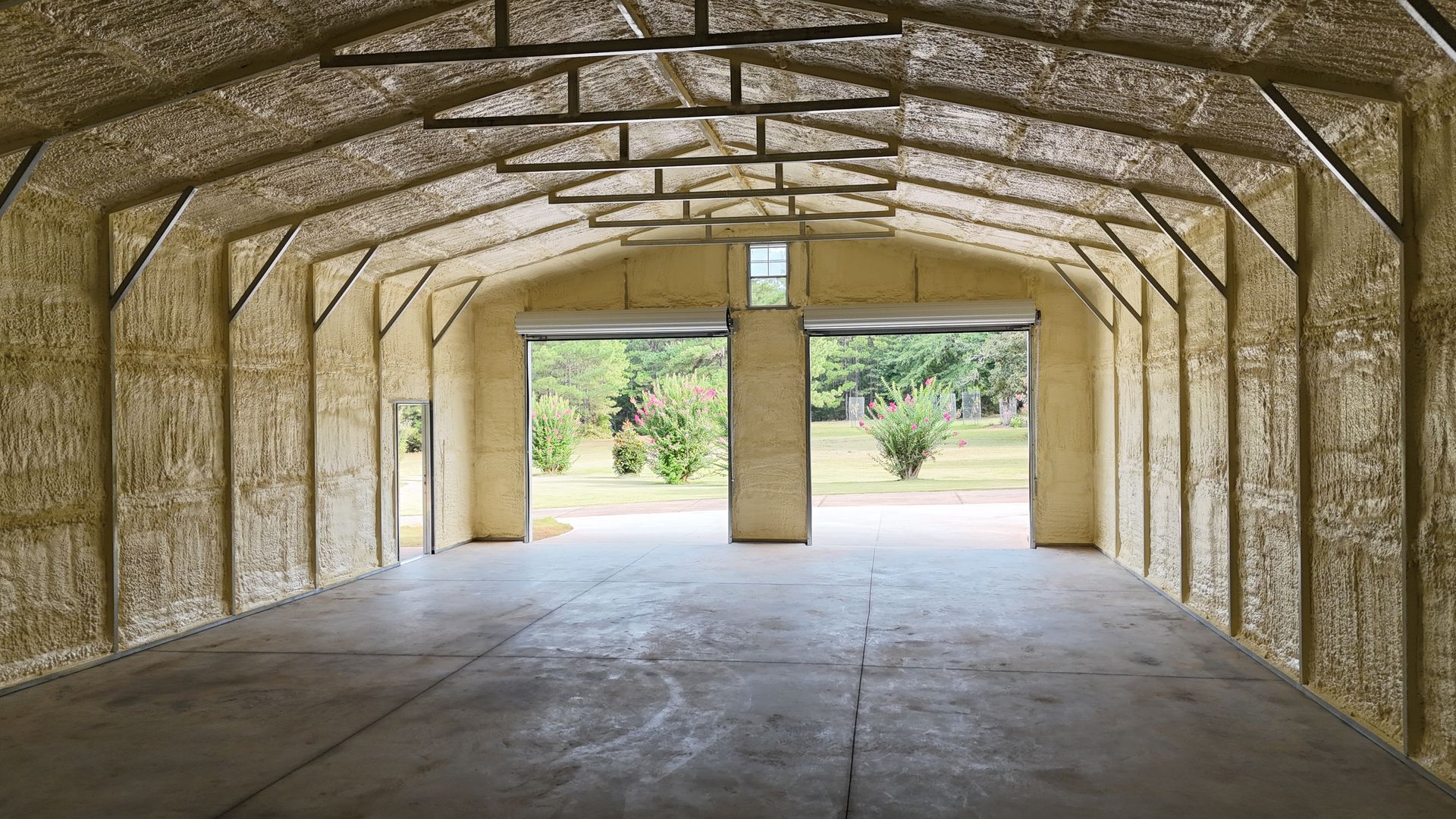 Empty arched barn interior with open doorway and daylight spilling onto a concrete floor