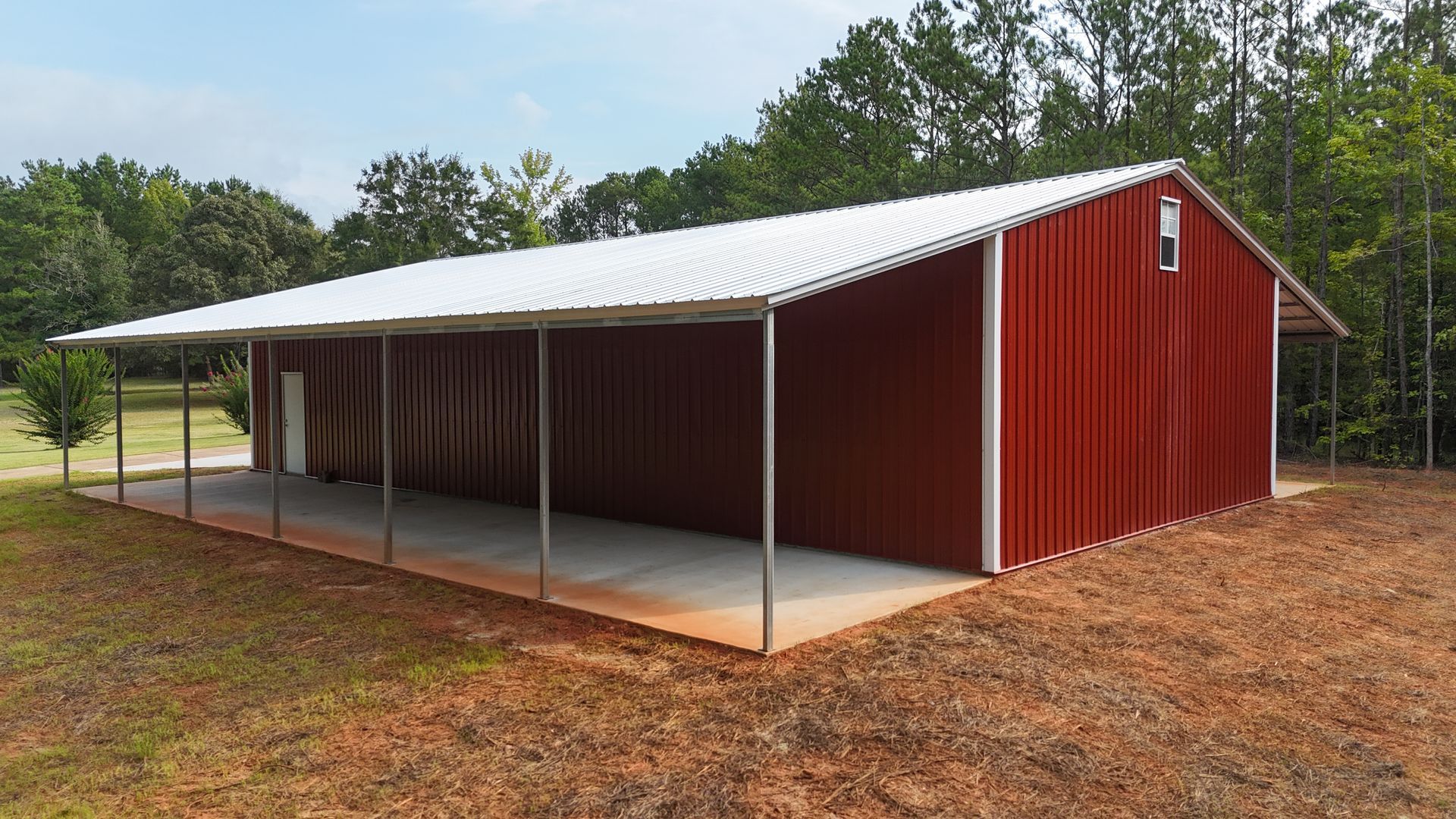 Red metal barn with white roof and open side in a rural wooded area
