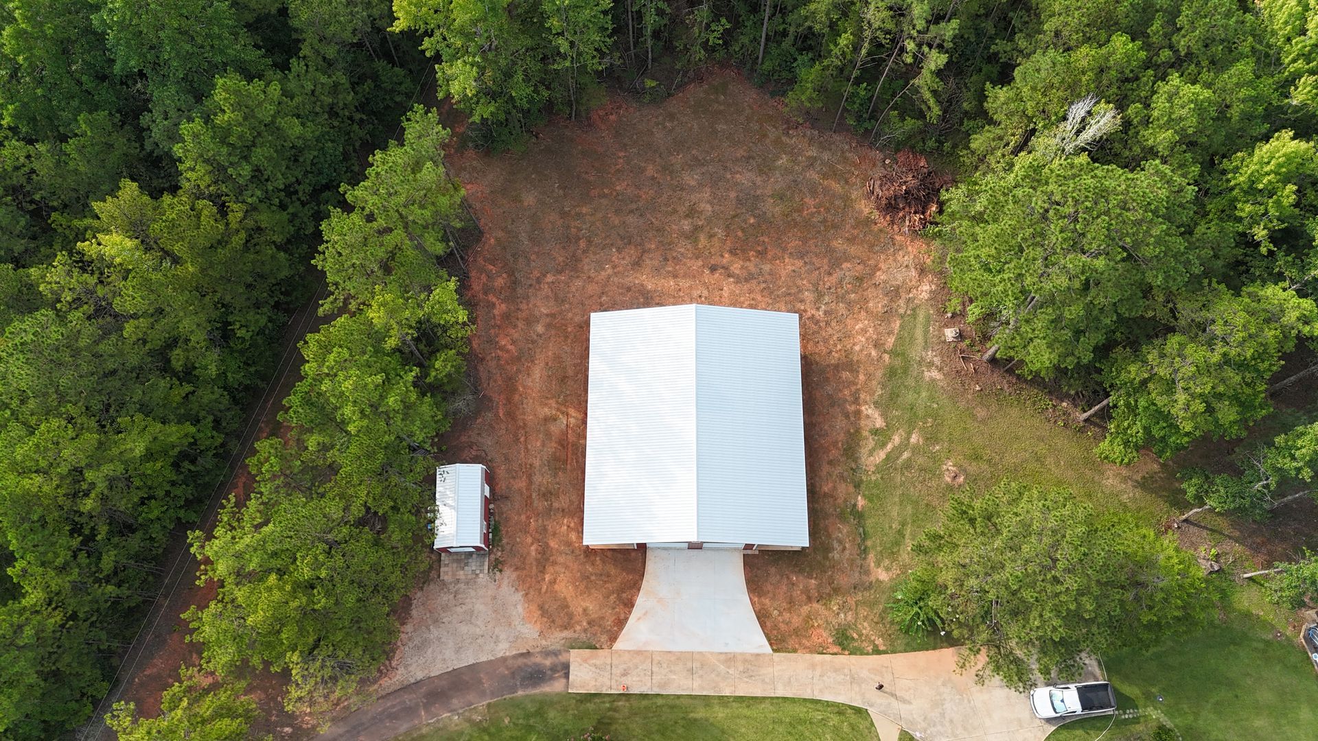 Aerial view of a white tent in a forest clearing with a small white vehicle nearby.