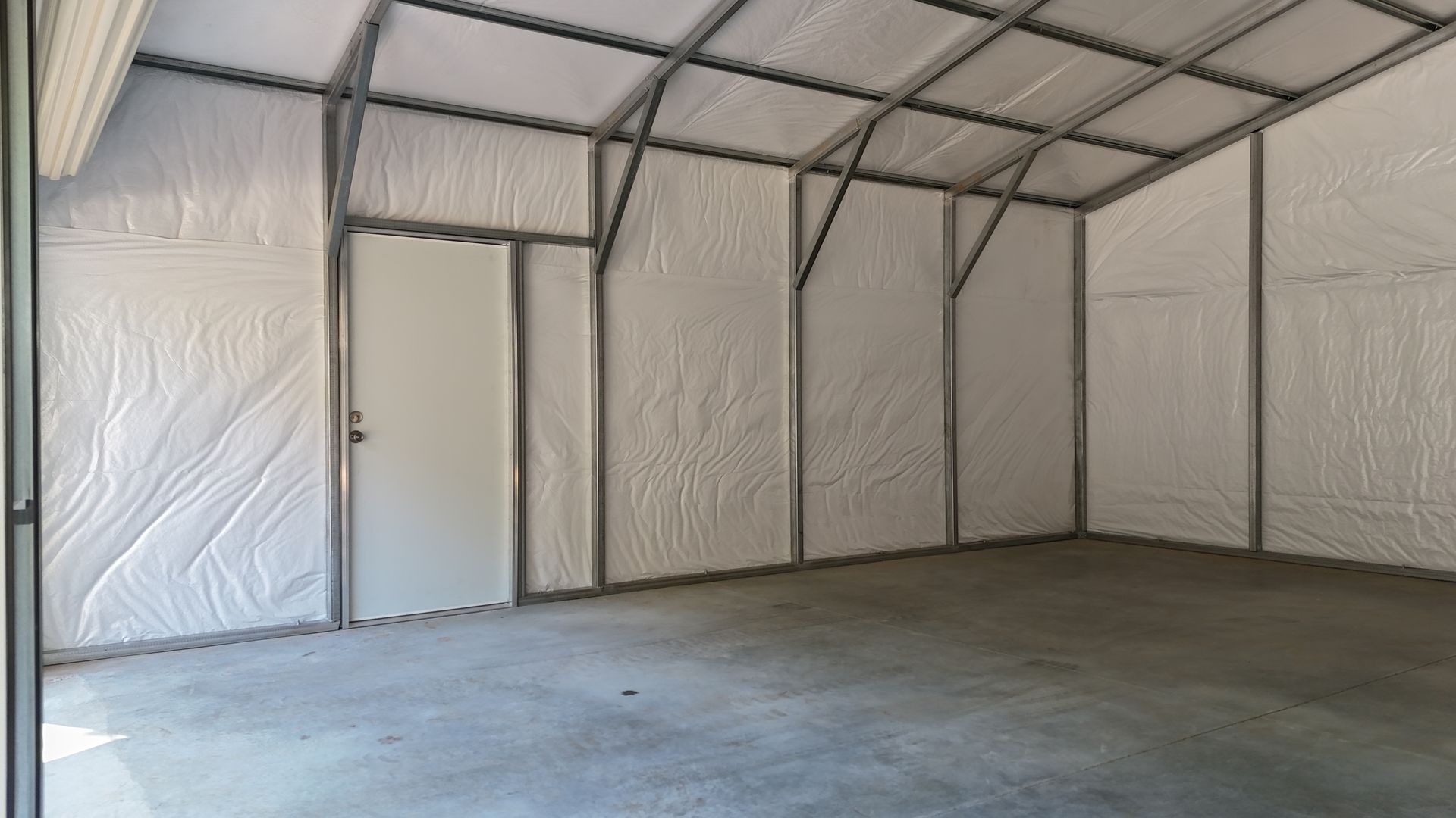 Empty metal-framed warehouse interior with insulated white walls and concrete floor