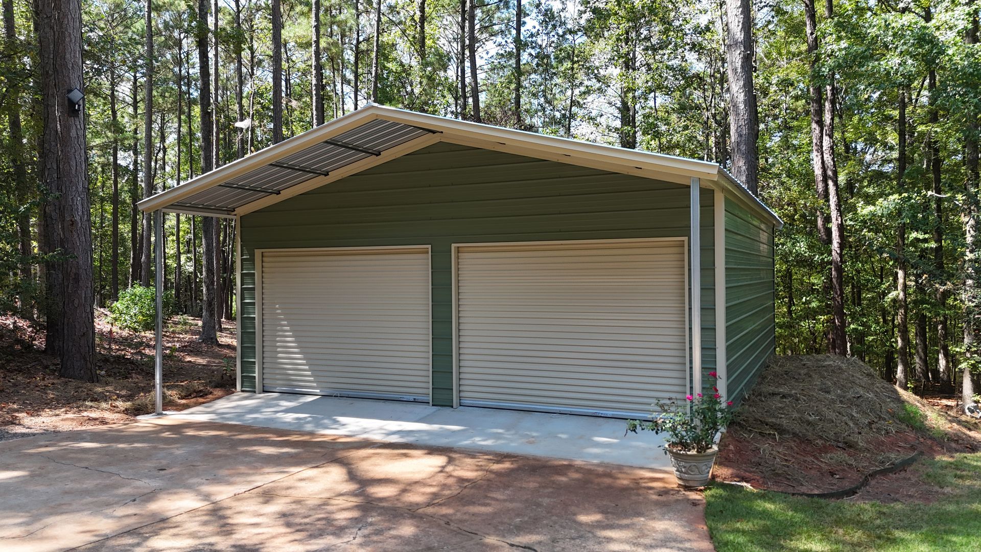 Two-car garage with white doors and green siding in a wooded driveway