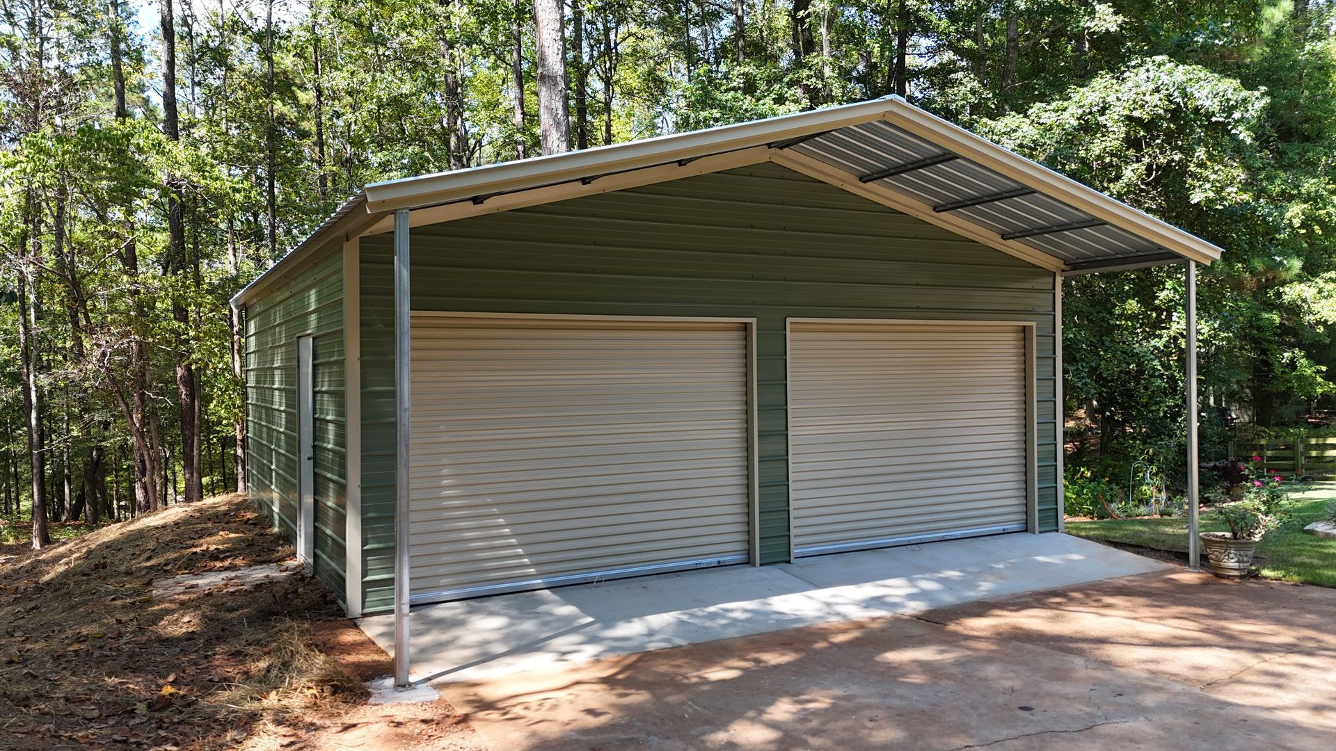 Two-car garage with white roll-up doors and a green metal roof in a wooded area