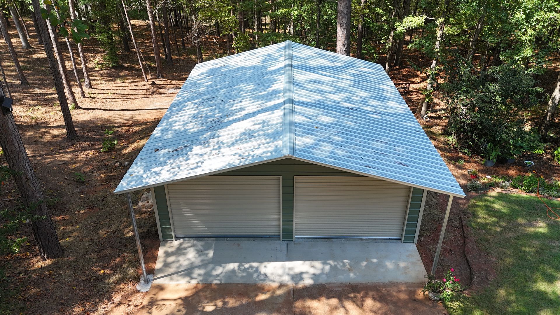 Small cabin with a blue metal roof in a wooded forest clearing, viewed from above.