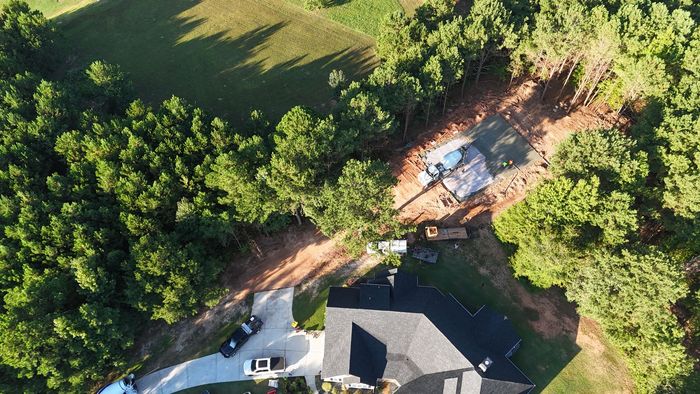 Aerial view of a wooded property with a house, driveway, and a blue vehicle parked near the trees.