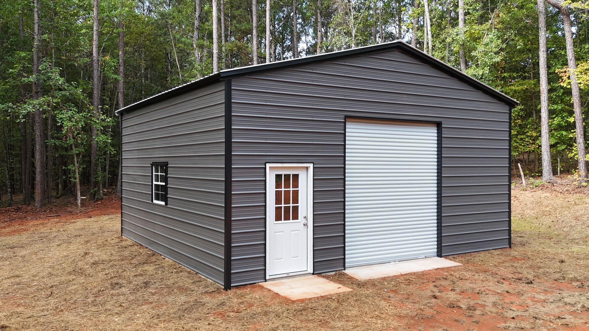 Gray metal shed with a white door and roll-up garage door in a wooded area