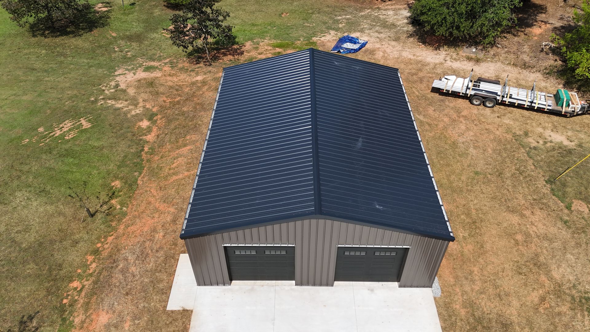 Aerial view of a new gray two-car garage with a dark blue roof and concrete driveway, surrounded by grass and trees
