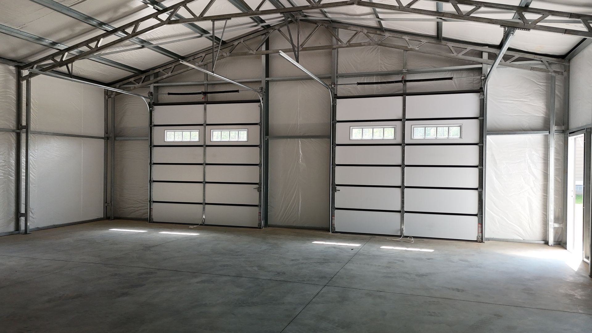 Empty industrial warehouse with concrete floor, metal walls, and two large garage doors
