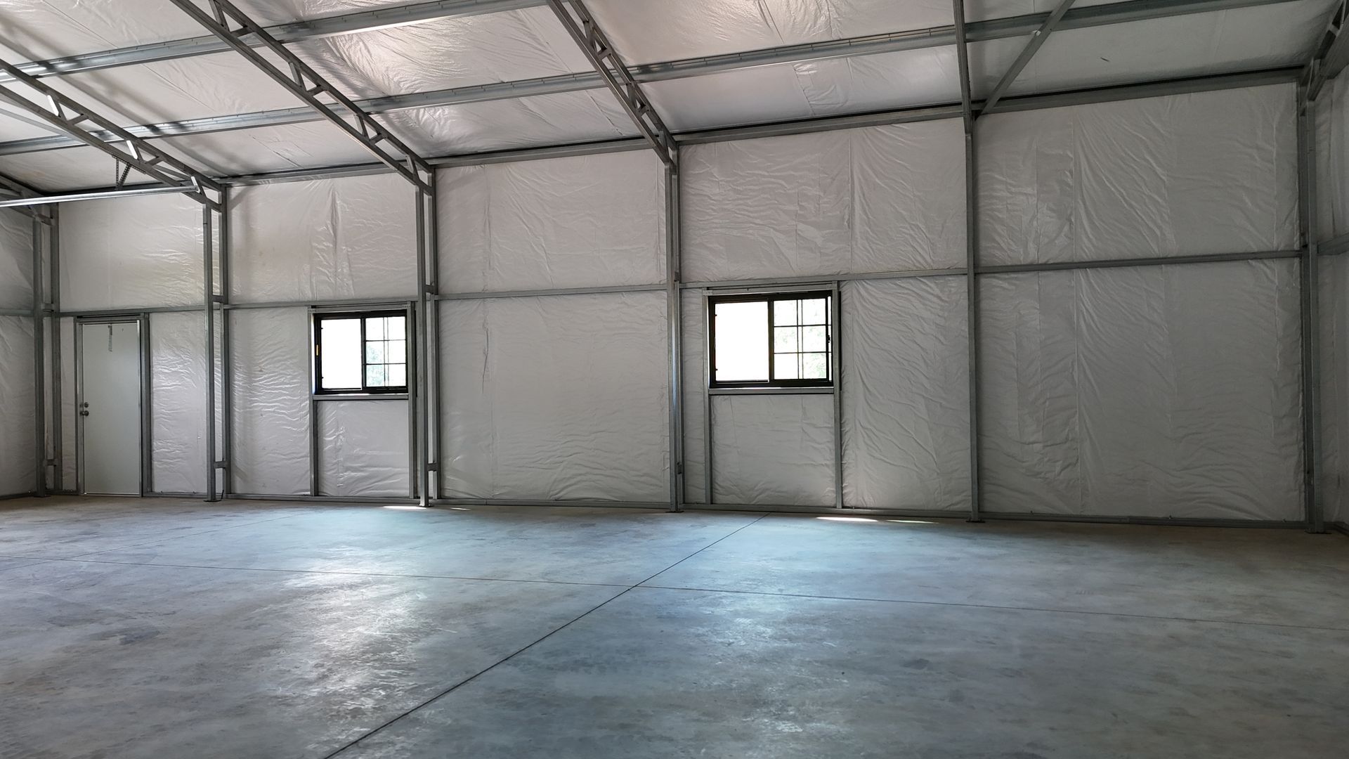 Empty industrial warehouse interior with metal walls, concrete floor, and two small windows