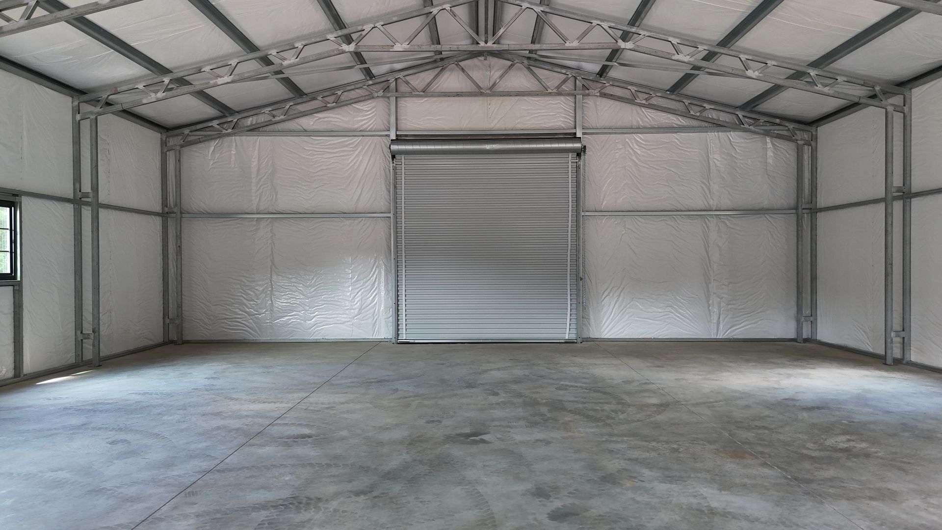 Empty metal warehouse interior with concrete floor and closed roll-up door