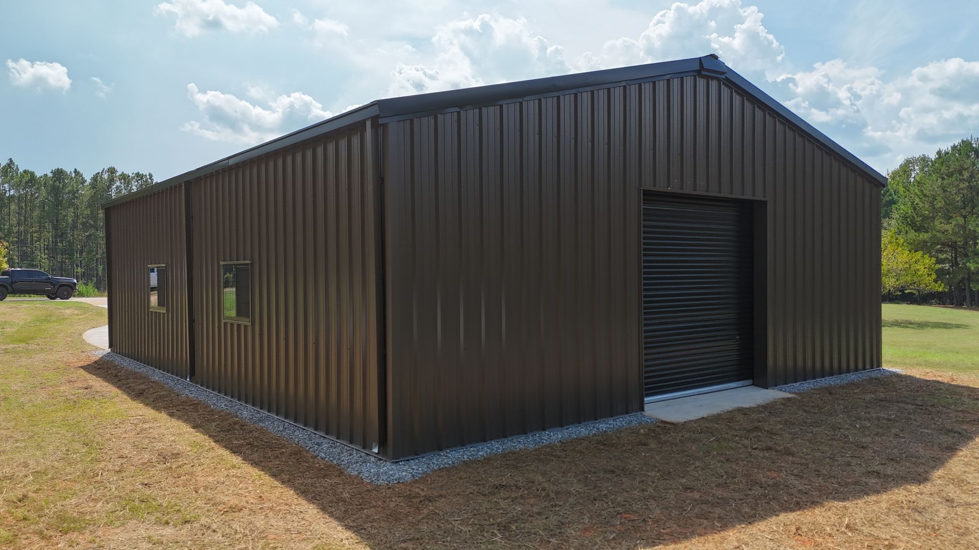 Brown metal barn-style warehouse with a large open roll-up door on a gravel lot