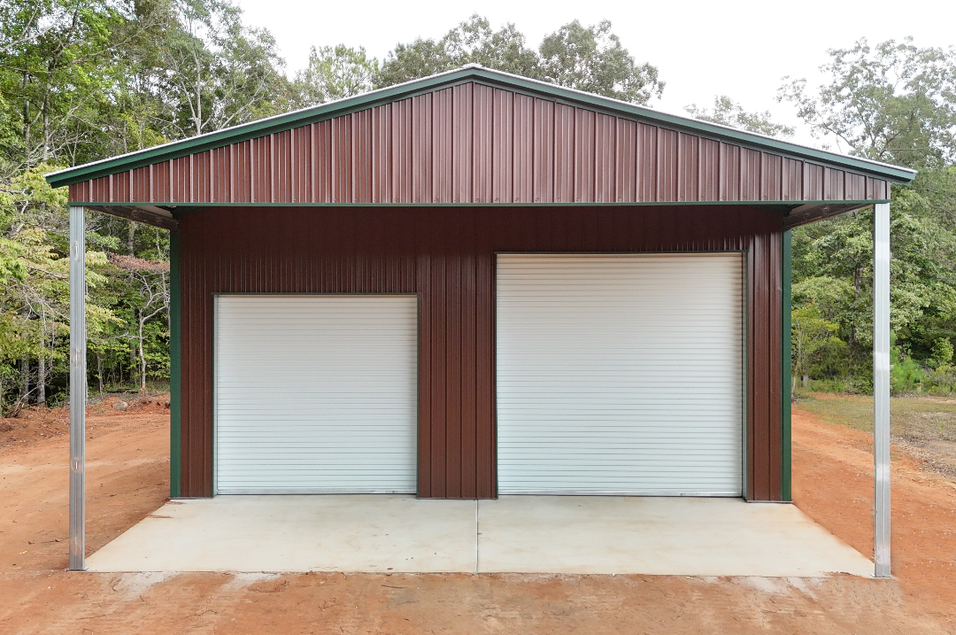 Brown metal garage with two white roll-up doors under a green-trimmed roof, set on a concrete slab.