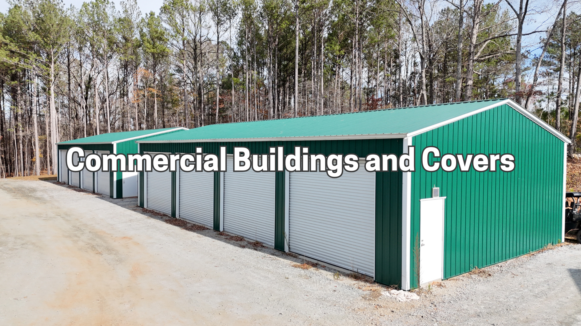 Green and white commercial storage building row beside a dirt road in a wooded area
