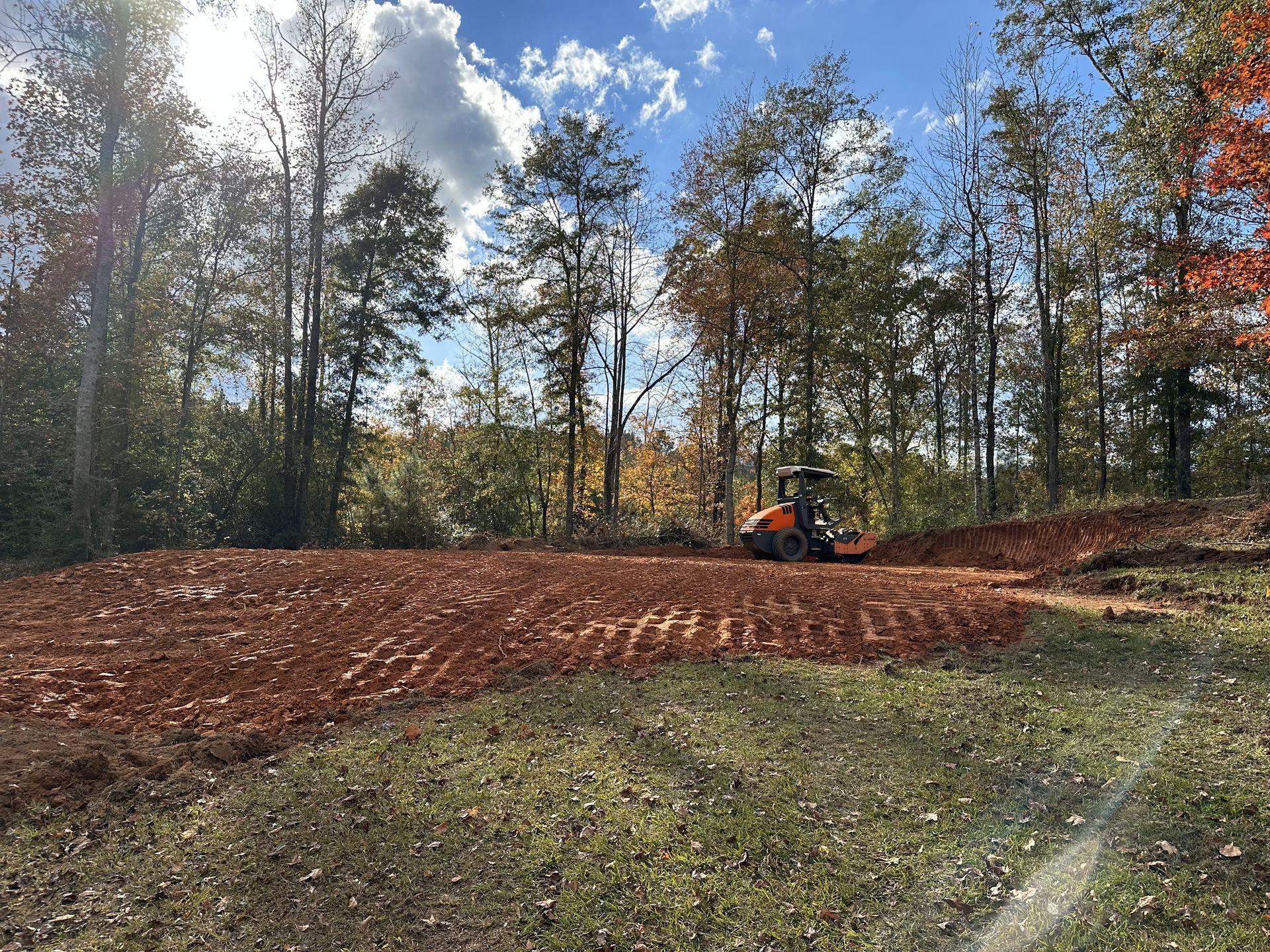 A tractor is plowing a dirt field in the middle of a forest.