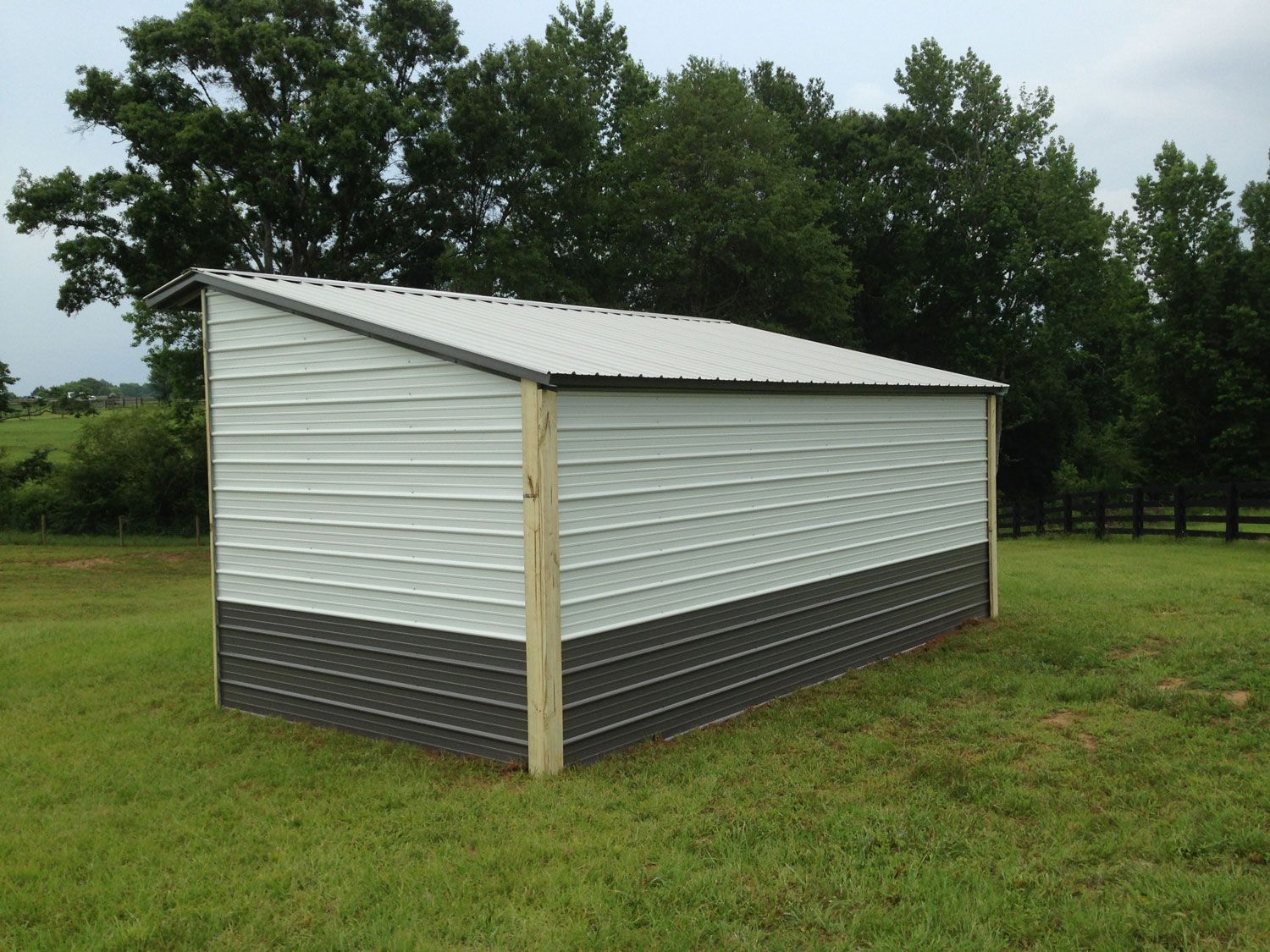 A white and black shed is sitting in the middle of a grassy field.