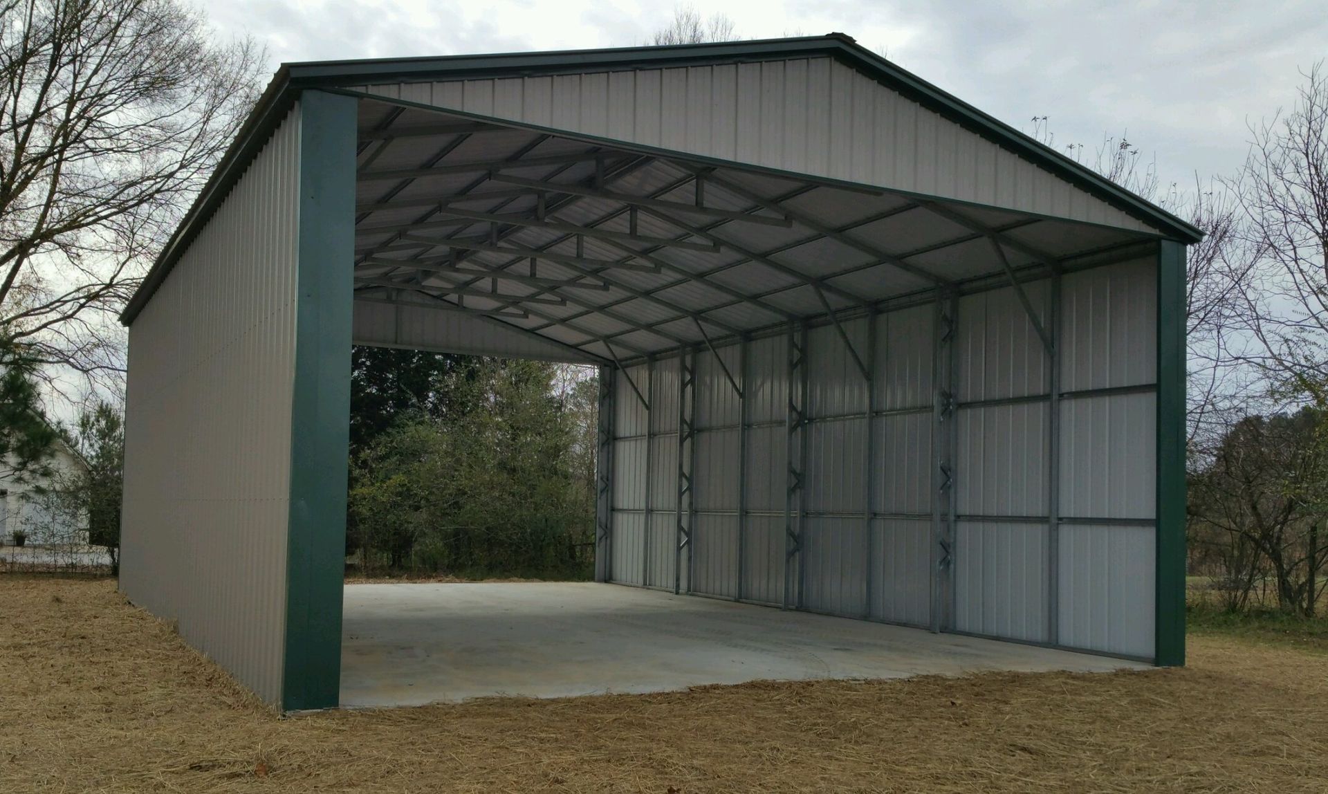 A large metal garage with a green roof is sitting on top of a dirt field.