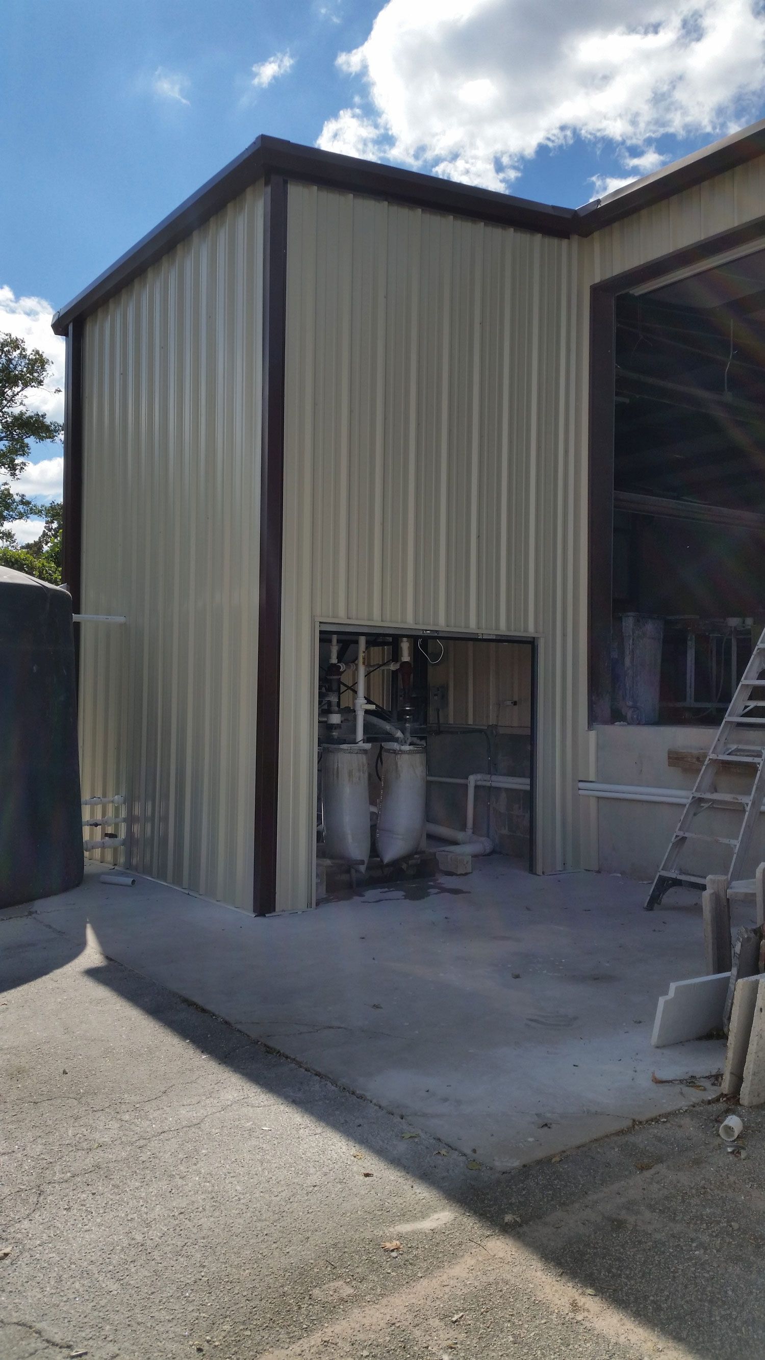 A metal building with a door open and a ladder in front of it.