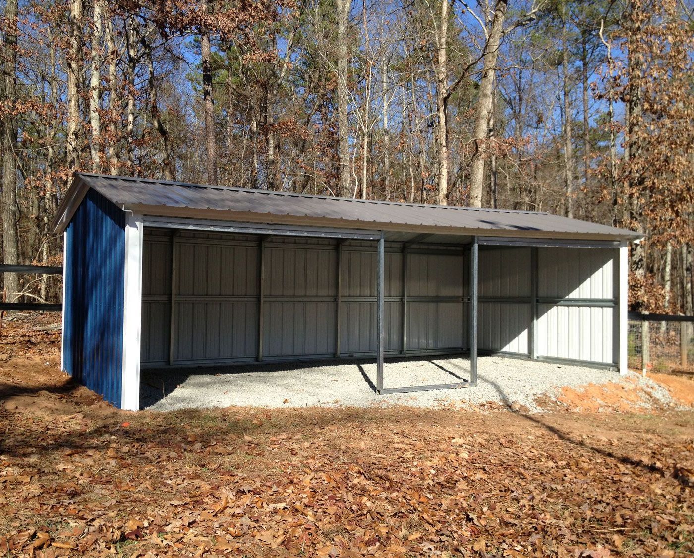 A blue and white barn is sitting in the middle of a forest.