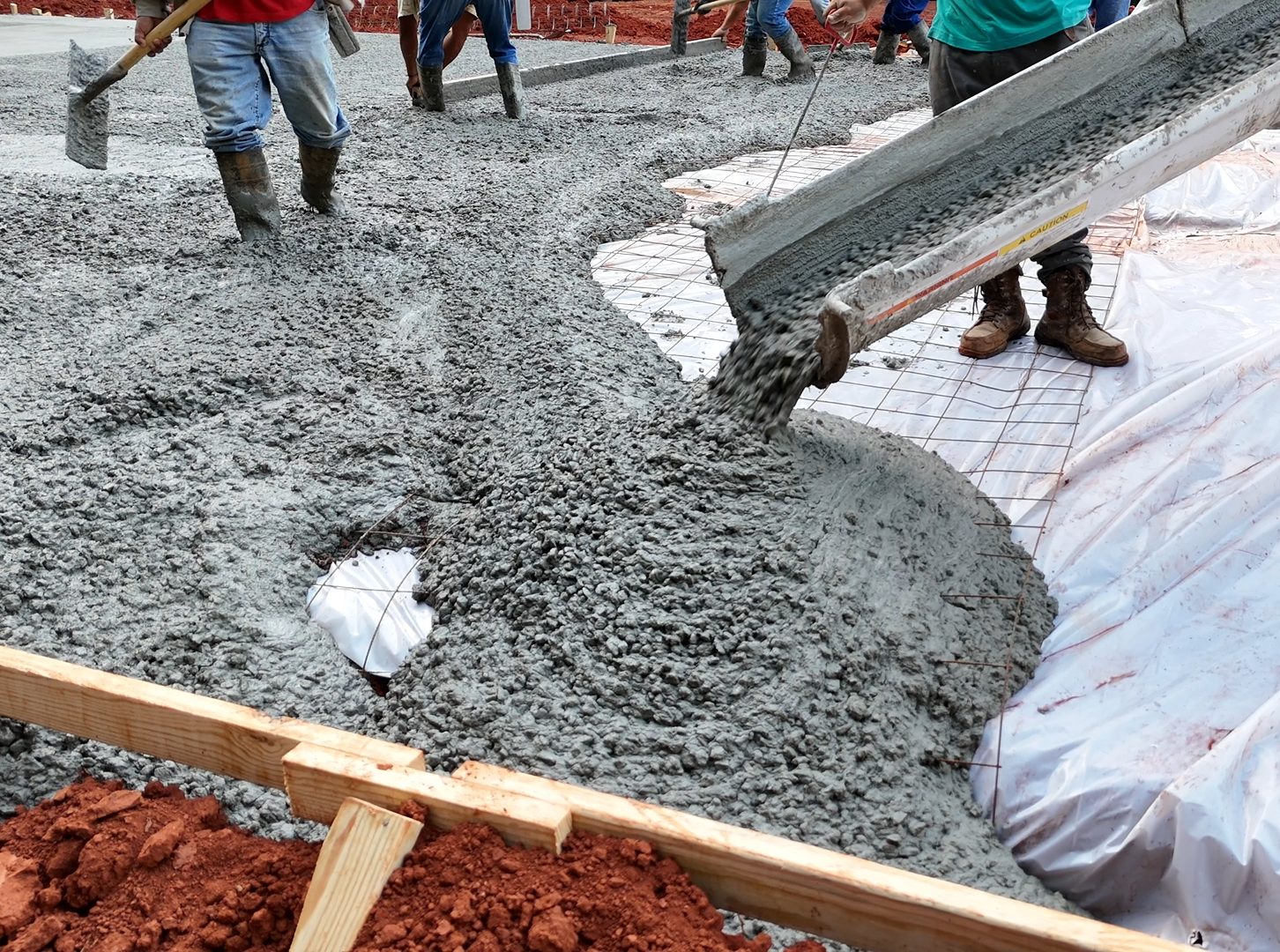 Concrete being poured from a chute onto a construction site. Workers in background.