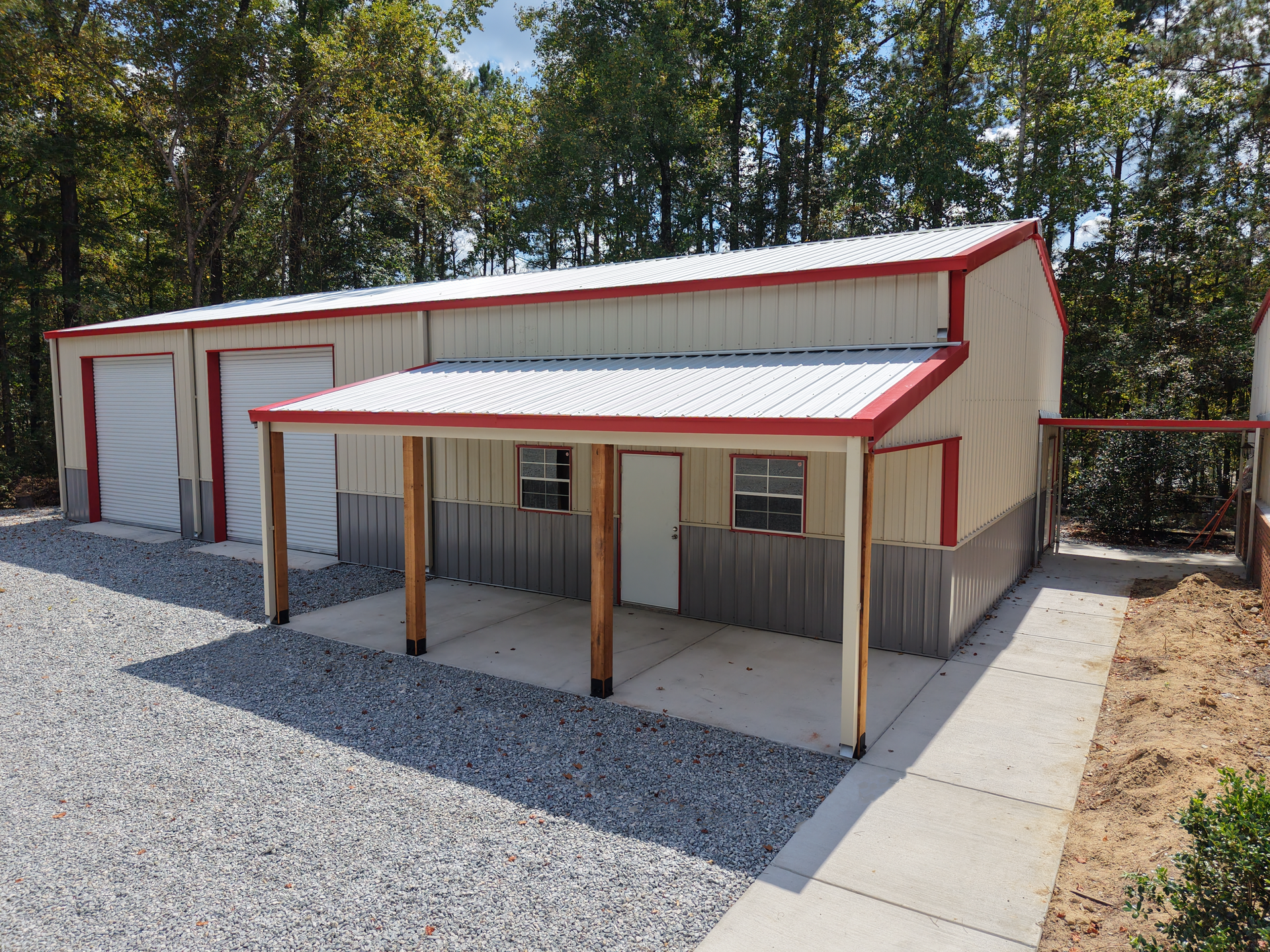 Red-and-white metal barn with a covered porch, gravel driveway, and trees in the background