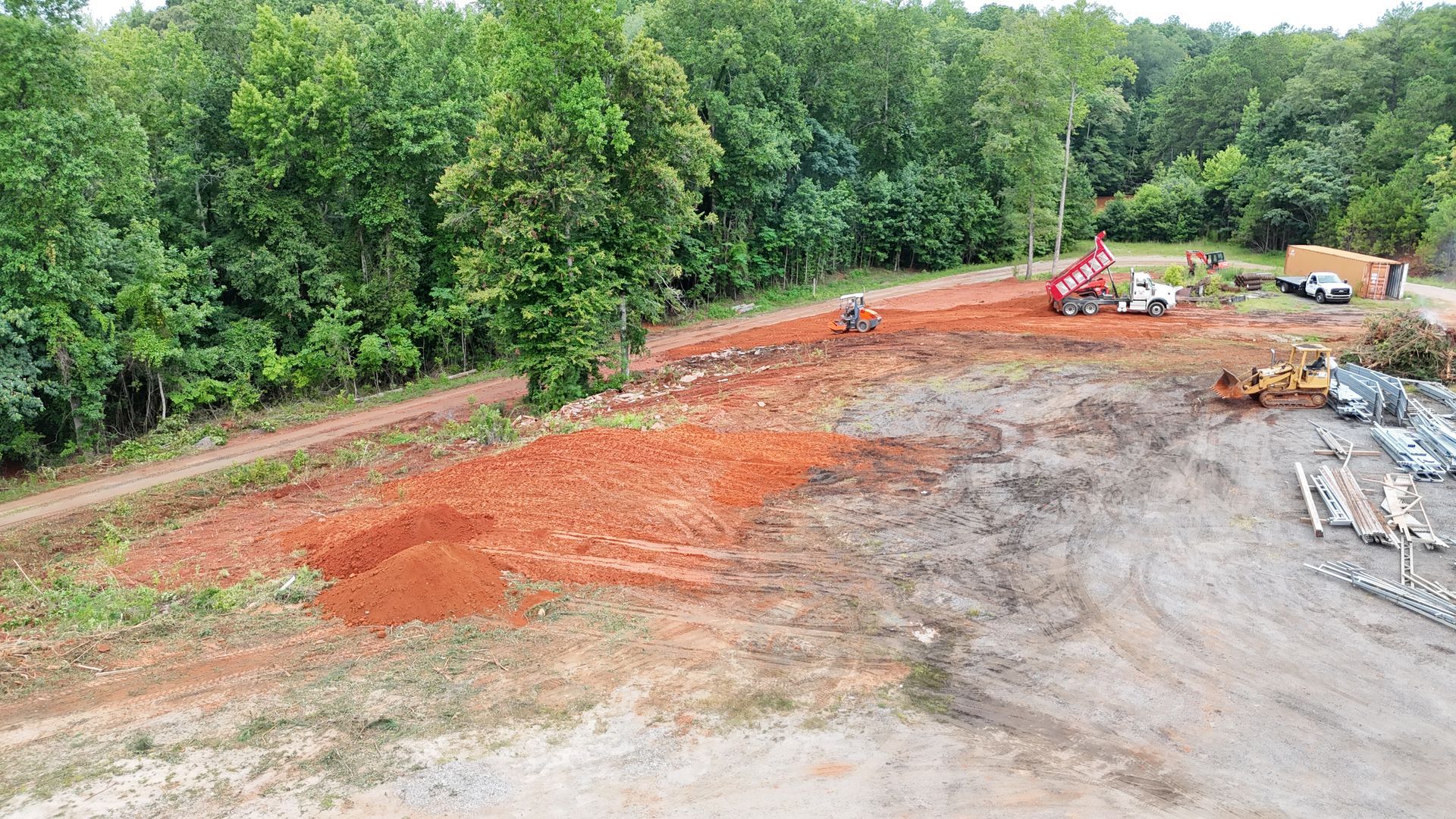 An aerial view of a construction site with a lot of dirt and trees in the background.