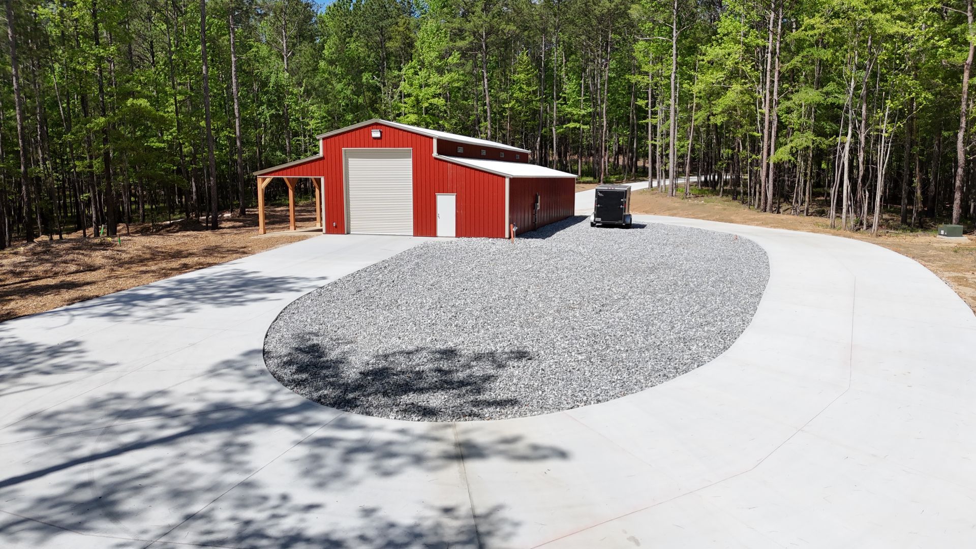 A red barn is sitting in the middle of a gravel driveway.