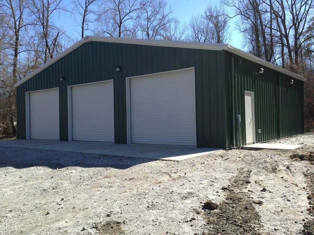 A green metal building with three white garage doors