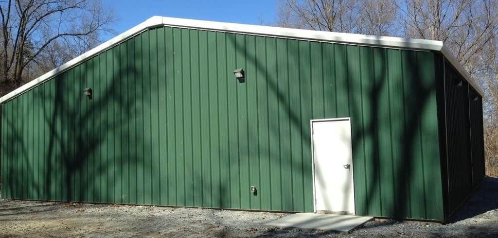 A green metal building with a white door and trees in the background.