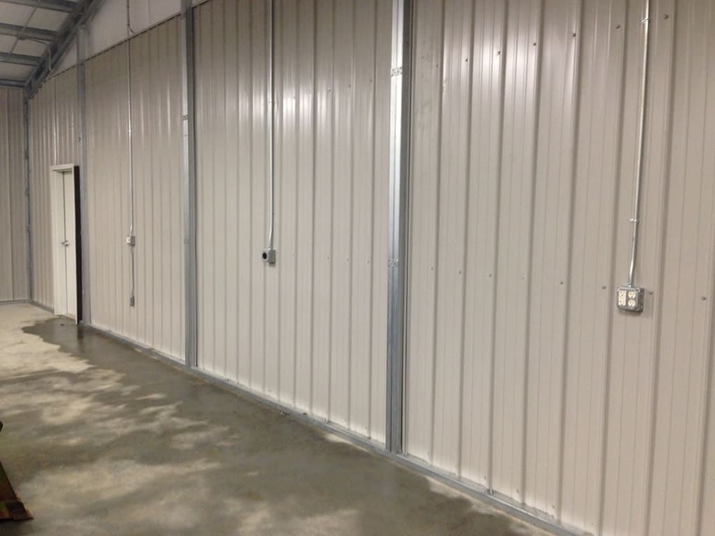 A long hallway in a building with white metal walls and a door.