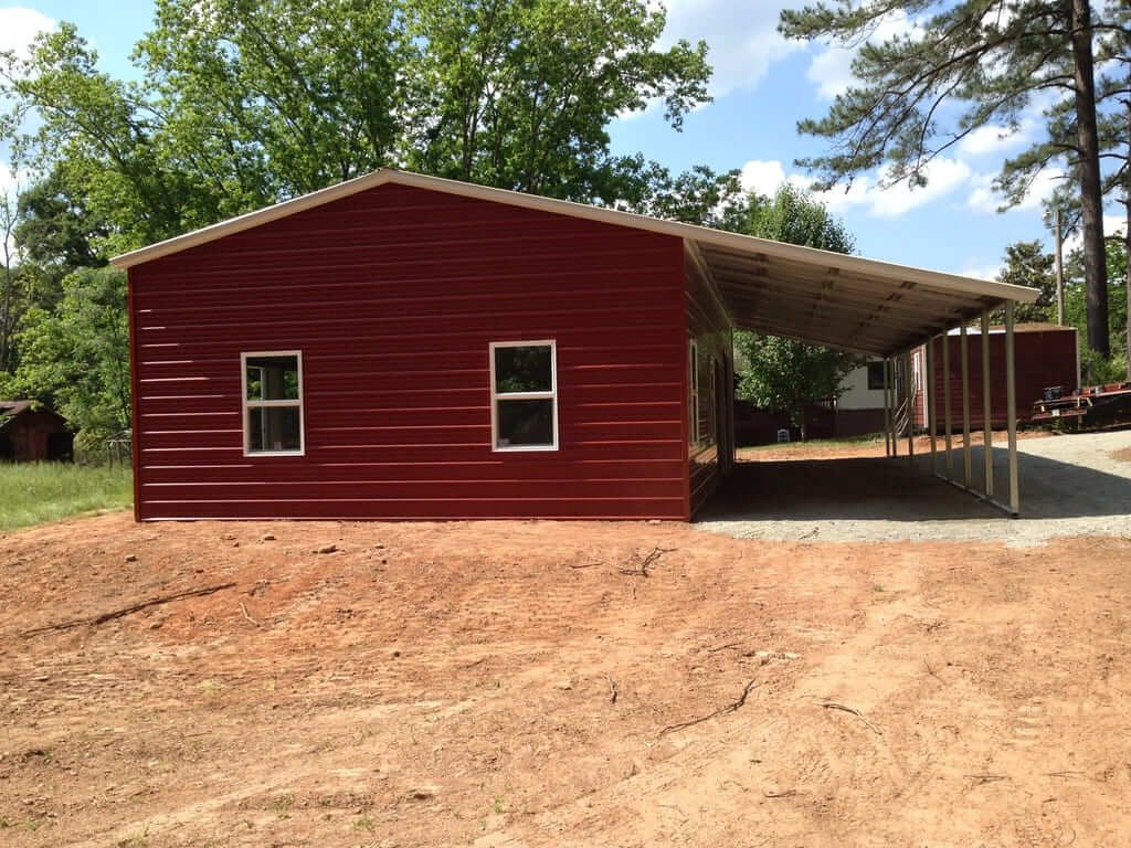 A red building with a carport underneath it in a dirt field.