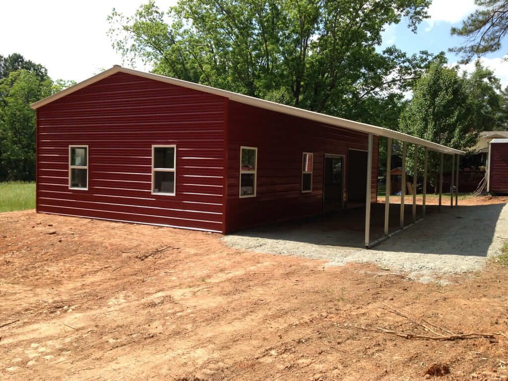 A red building with a white roof is sitting in the middle of a dirt field.