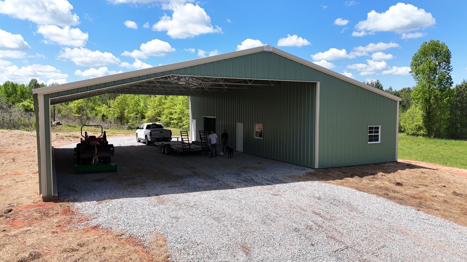 A green metal building with a tractor parked underneath it.