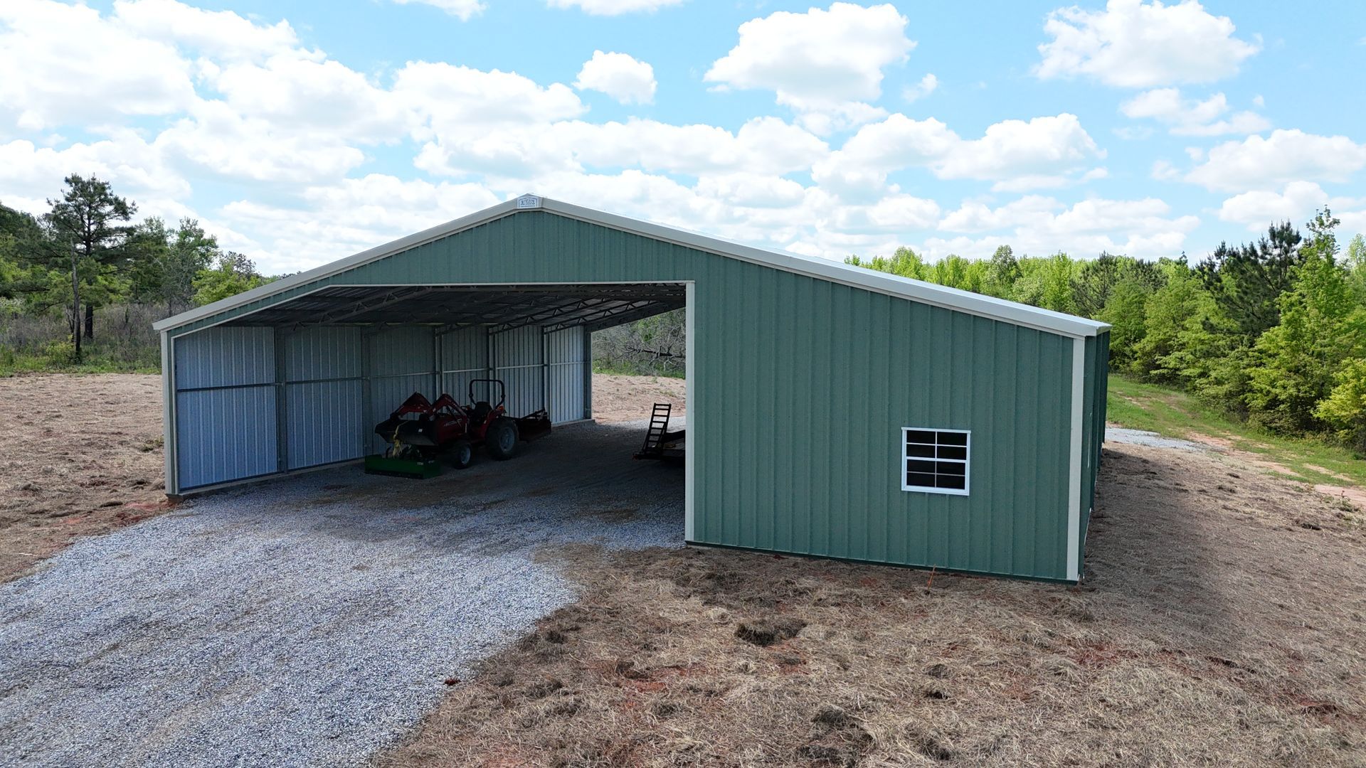 A green metal building with a tractor parked inside of it.