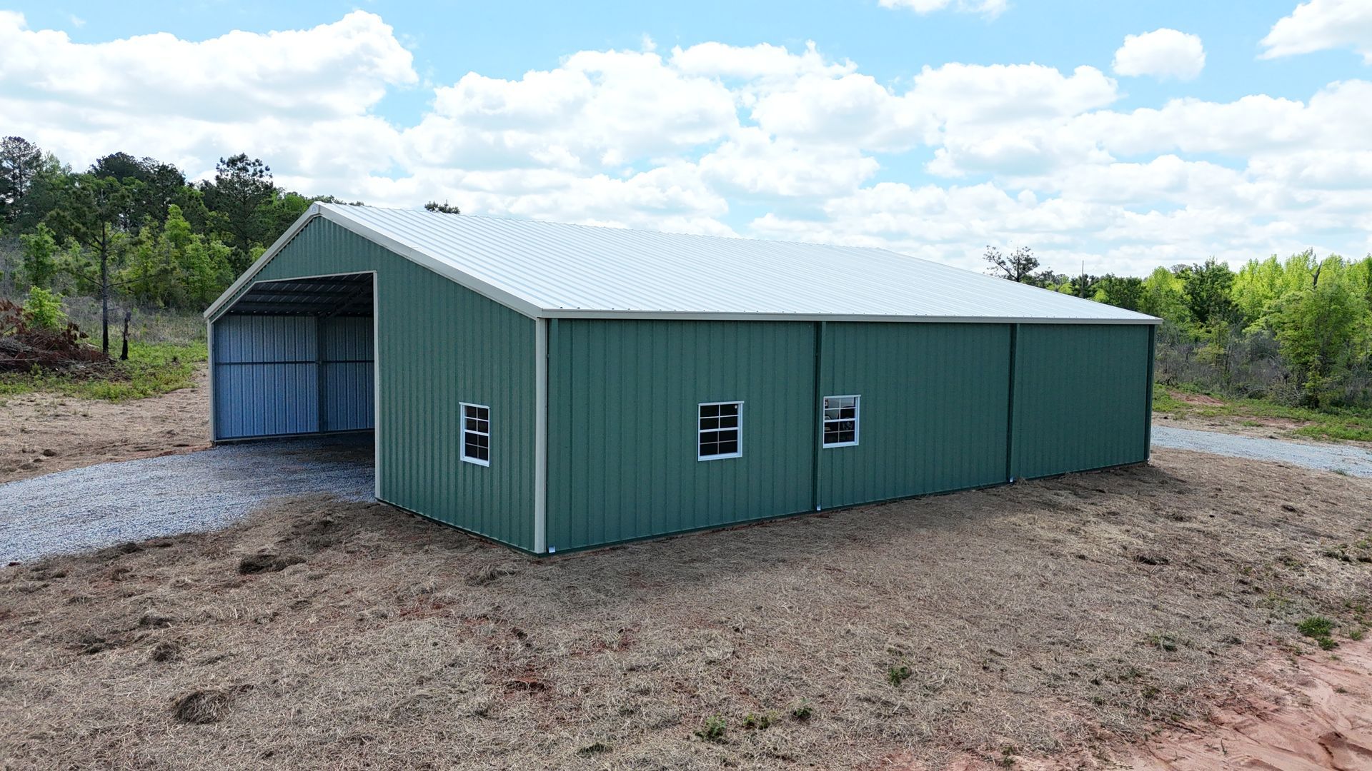 A green metal building with a white roof is sitting in the middle of a dirt field.