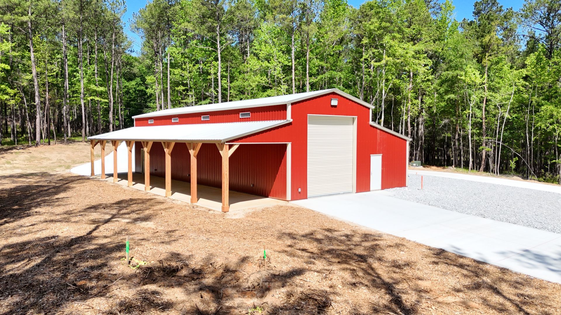 A red barn with a white roof is in the middle of a forest.