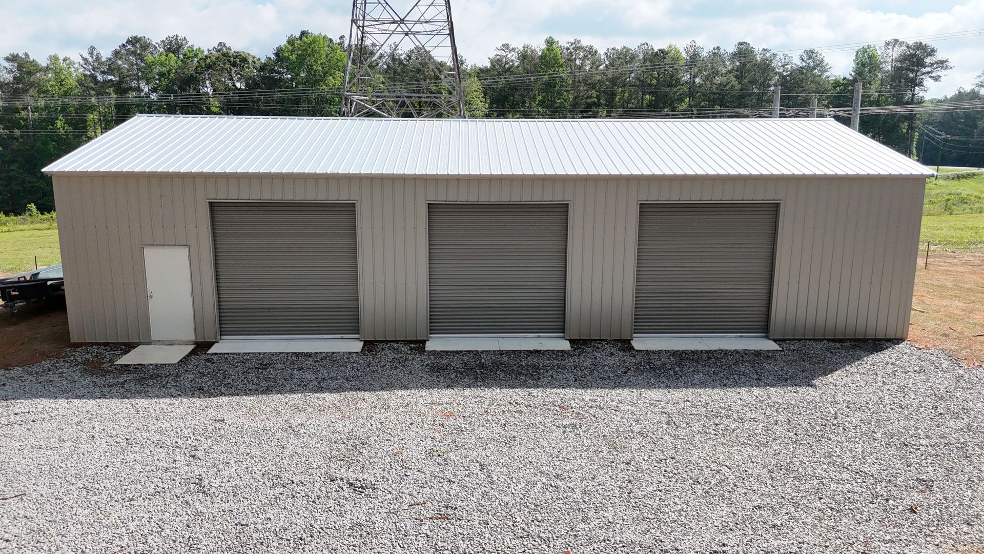 A large building with three garage doors is sitting on top of a gravel lot.