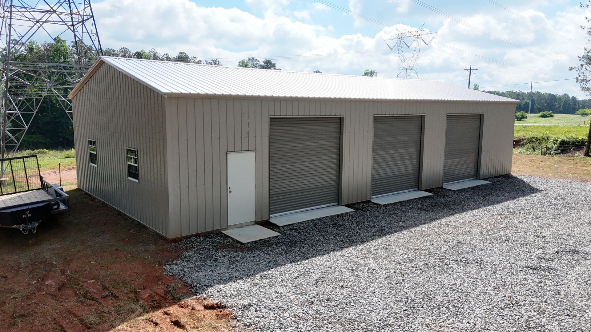 A large metal building with three garage doors and a trailer parked in front of it.