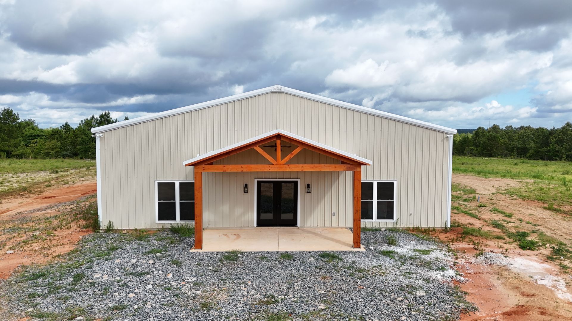 A large white building with a wooden porch is sitting in the middle of a dirt field.
