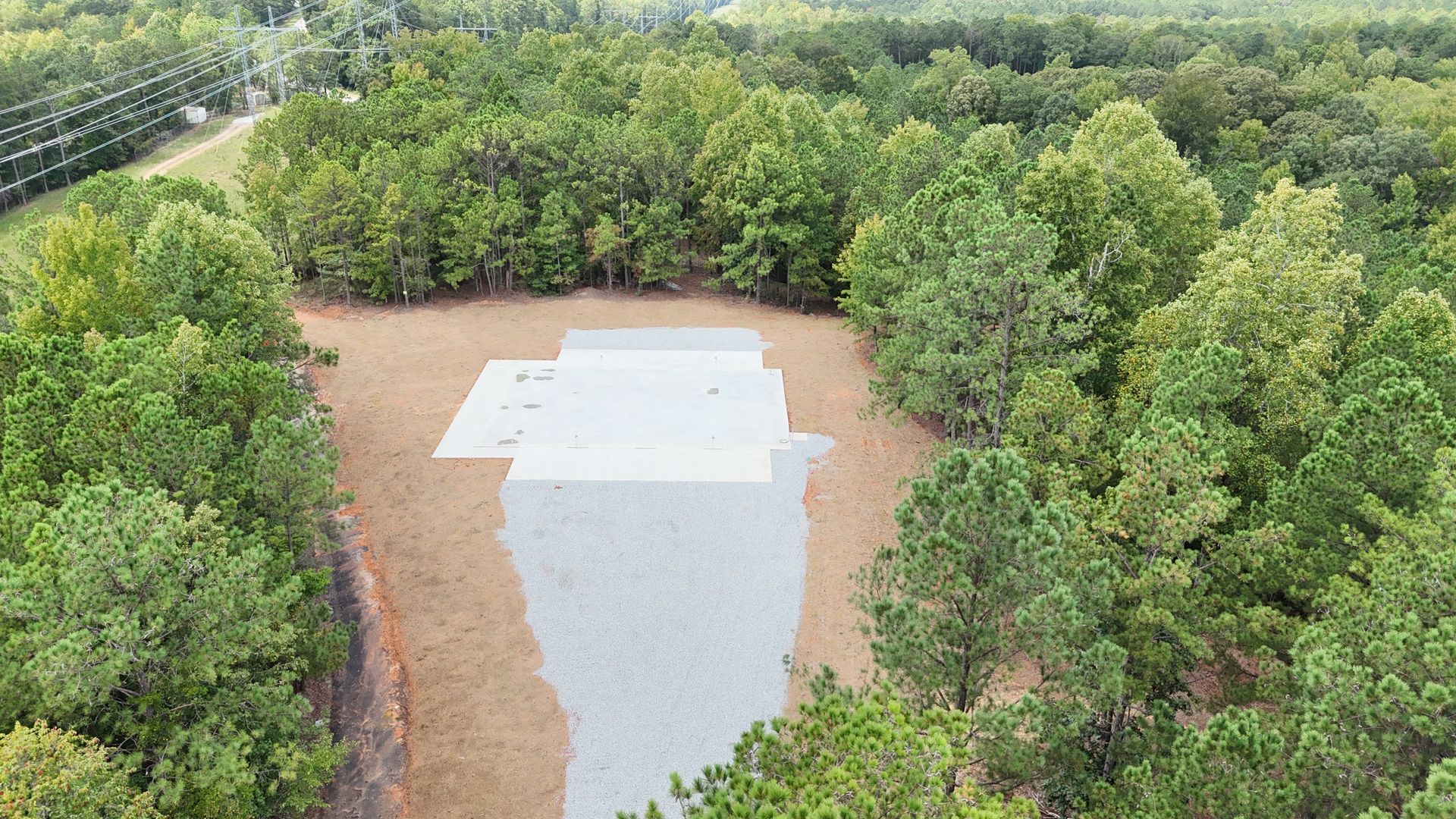 Aerial view of a large gray concrete slab clearing surrounded by dense green trees.